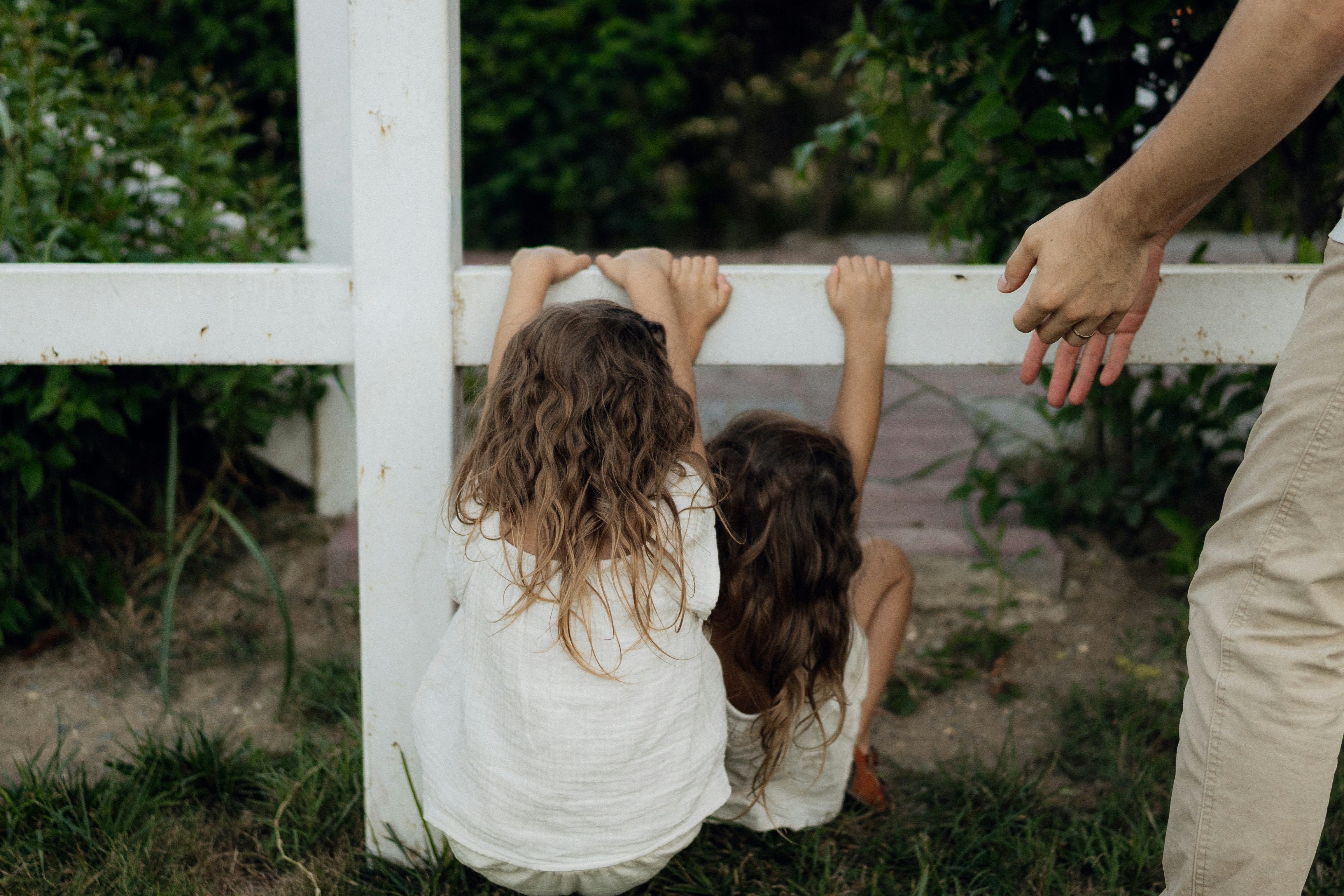 Two children climb over a white fence outdoors.