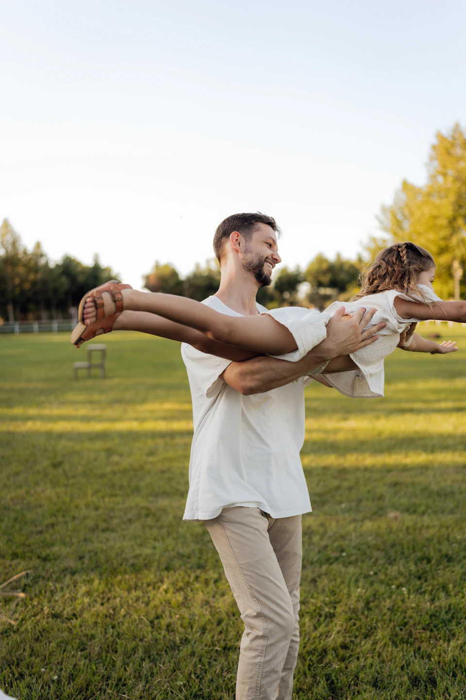 A father swinging his laughing daughter like an aeroplane in a sunny park