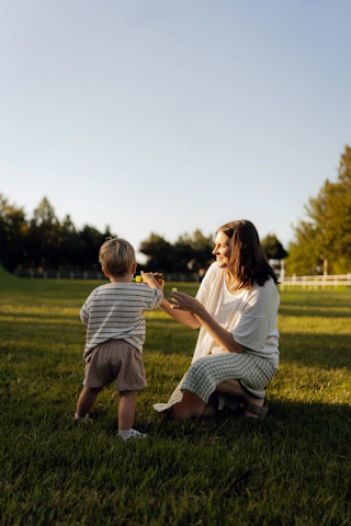 Mother and son blowing bubbles in a grassy field.