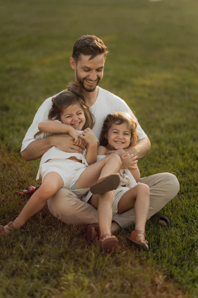 Father smiling with two laughing daughters on grass