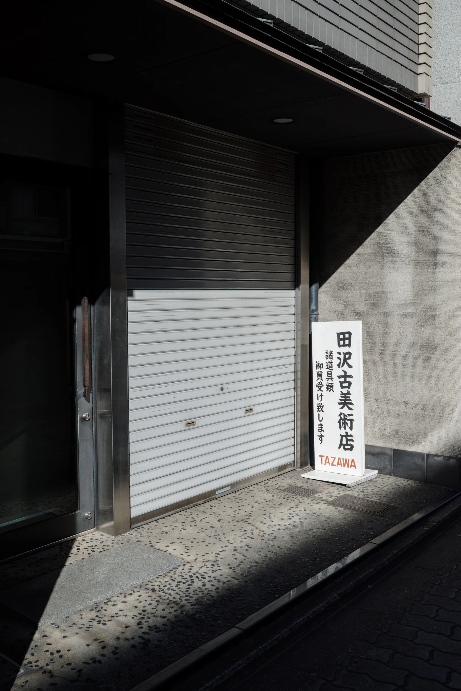 A storefront with its metal roller shutter pulled fully closed at dusk, illustrating a market shut for the weekend with no way to manage an open position until it reopens