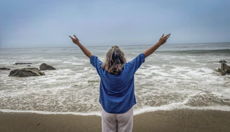 Woman with arms raised on a beach facing ocean
