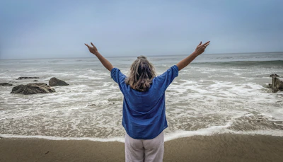 Woman with arms raised on a beach facing ocean