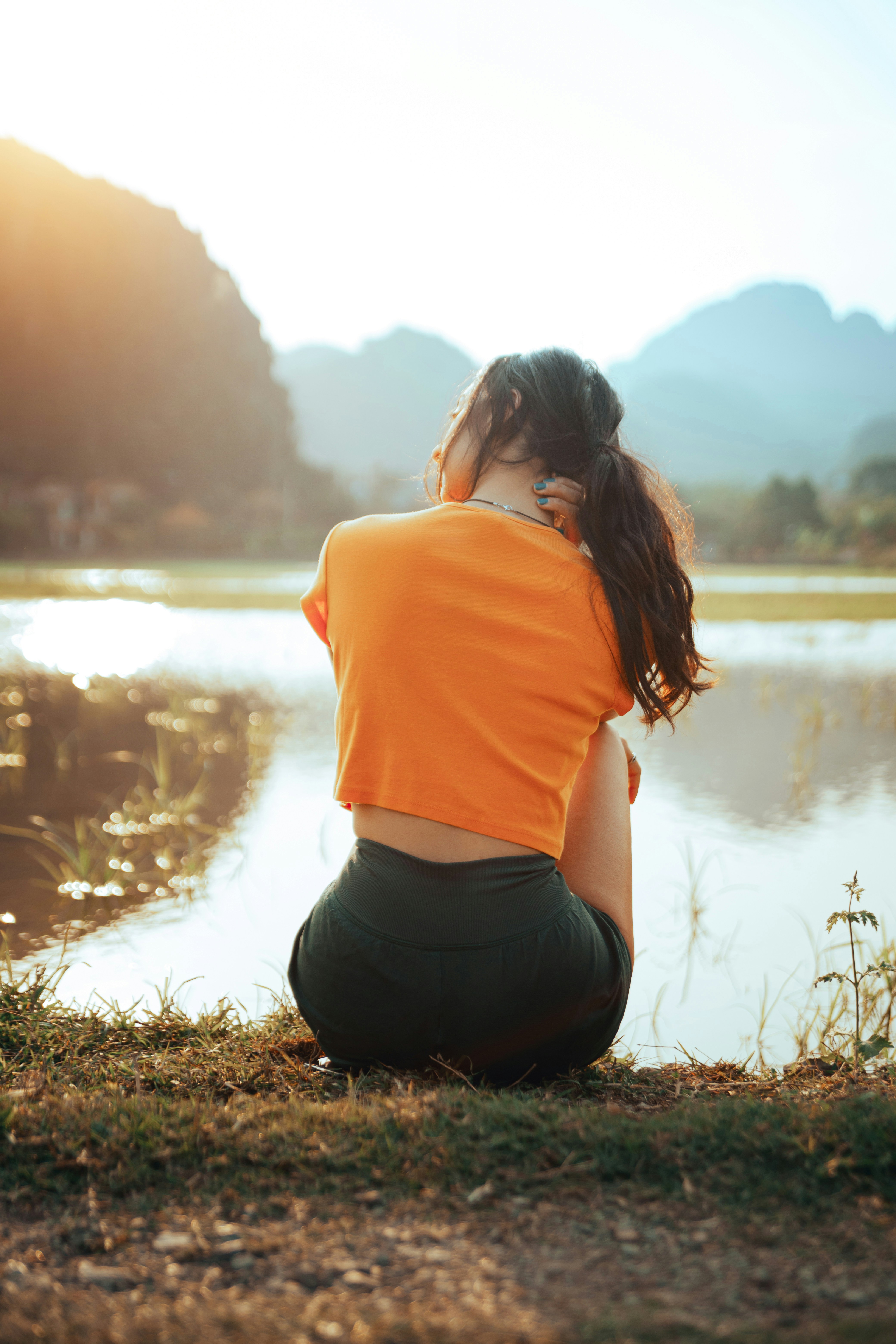 Woman sitting by water with mountains in background.