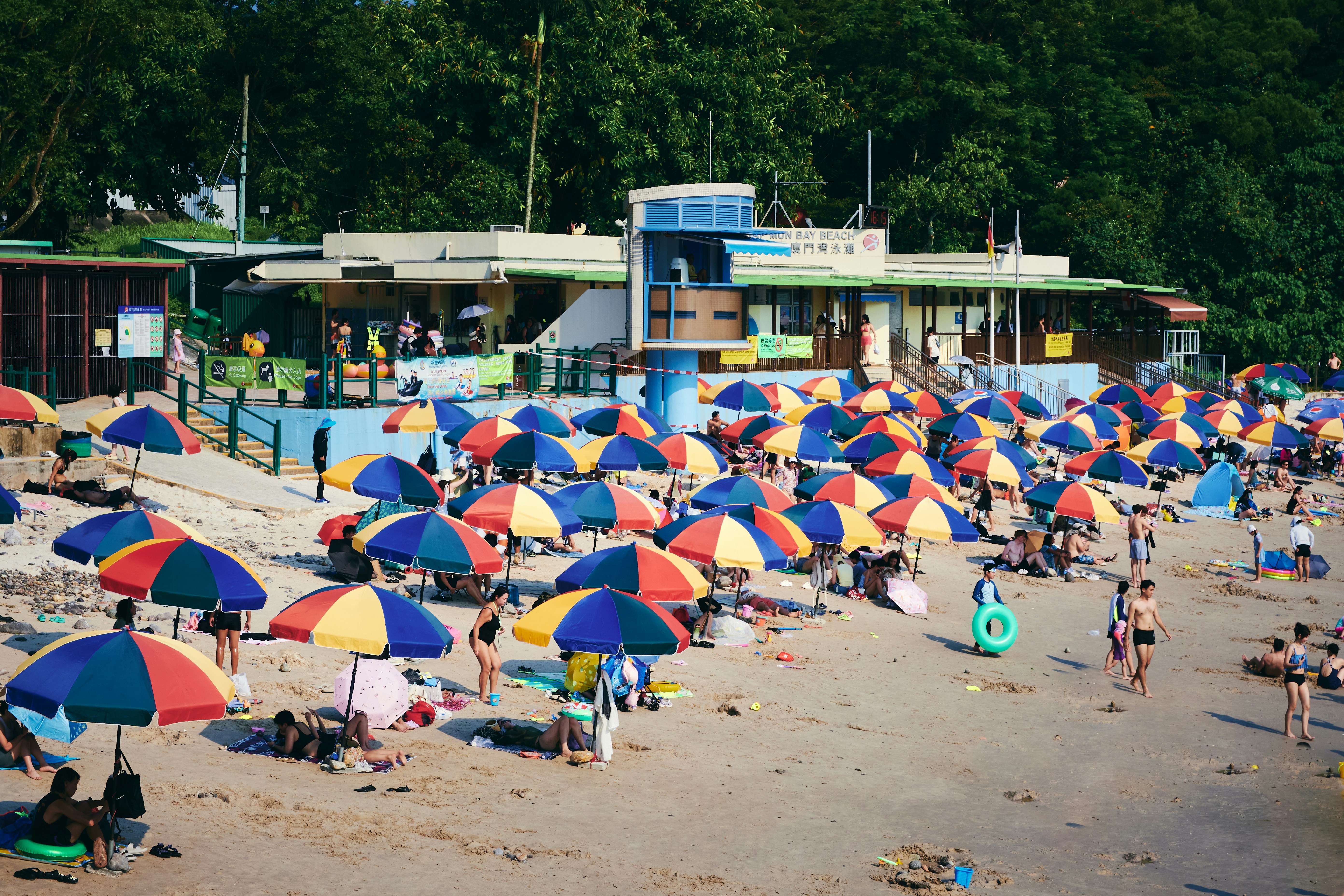 Crowded beach with colorful umbrellas and a building.