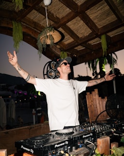 Dj with arms raised playing music at sunset
