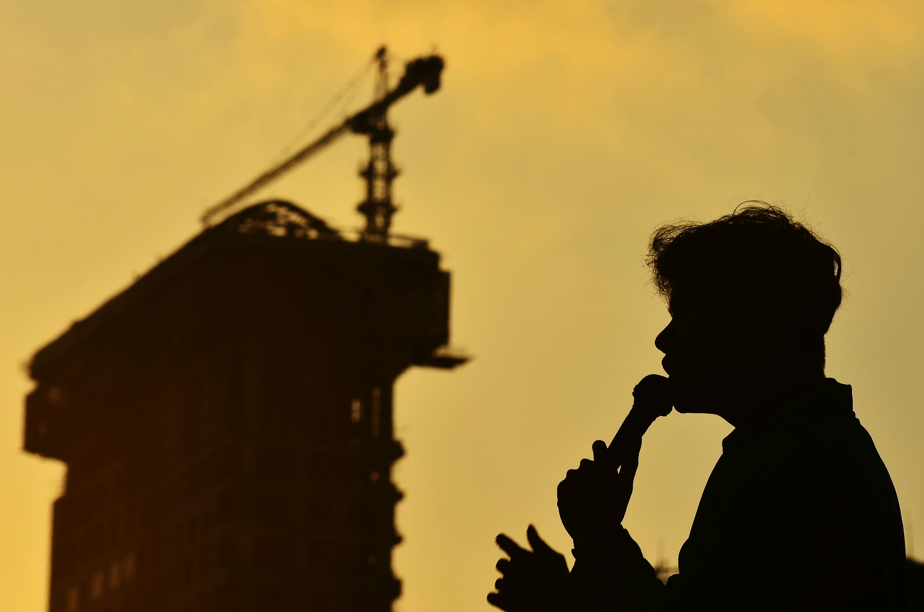 Silhouette of a person speaking with a building and crane.