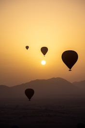 Hot air balloons float across a hazy sunset sky.