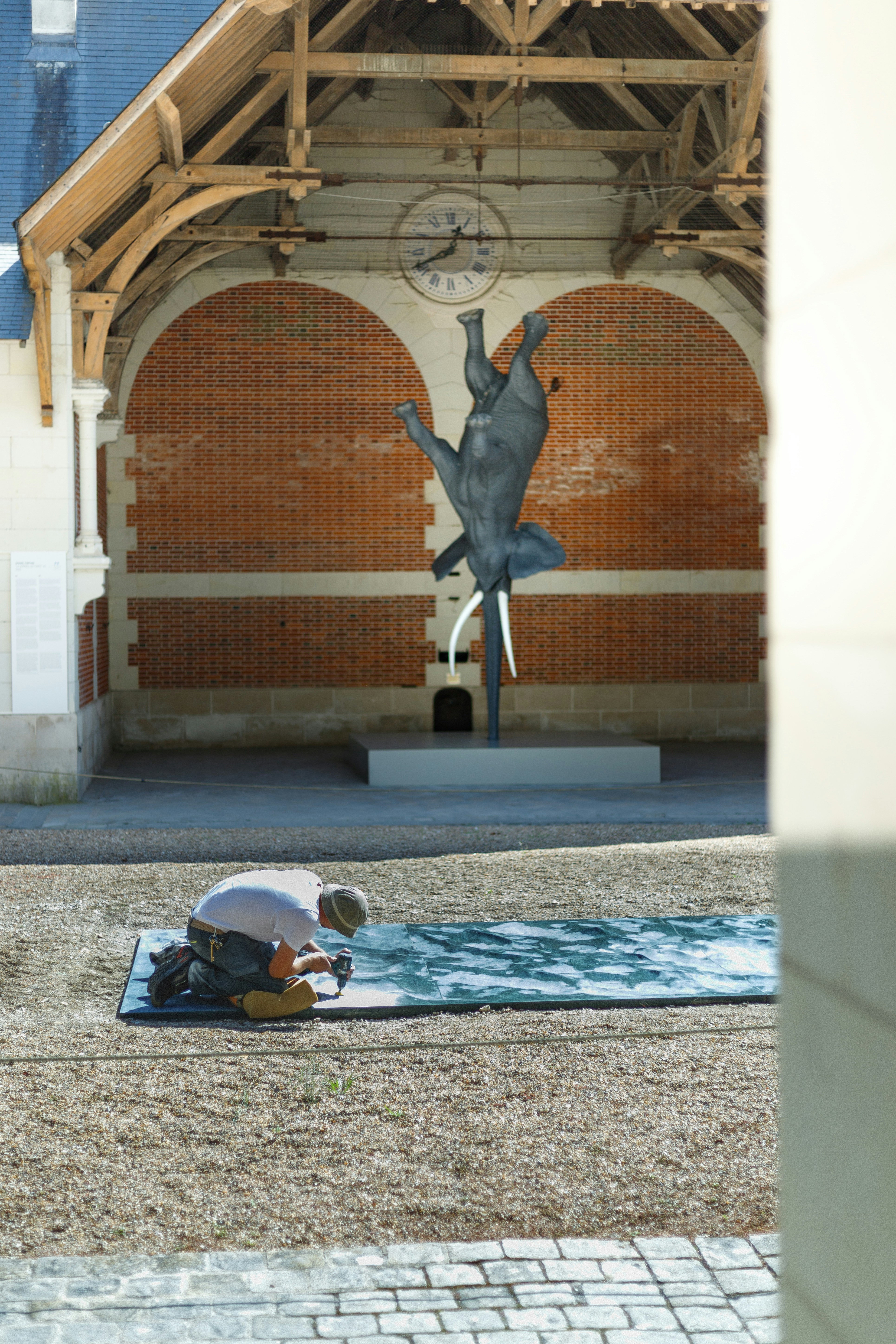 Man kneeling on mat before upside down elephant sculpture.