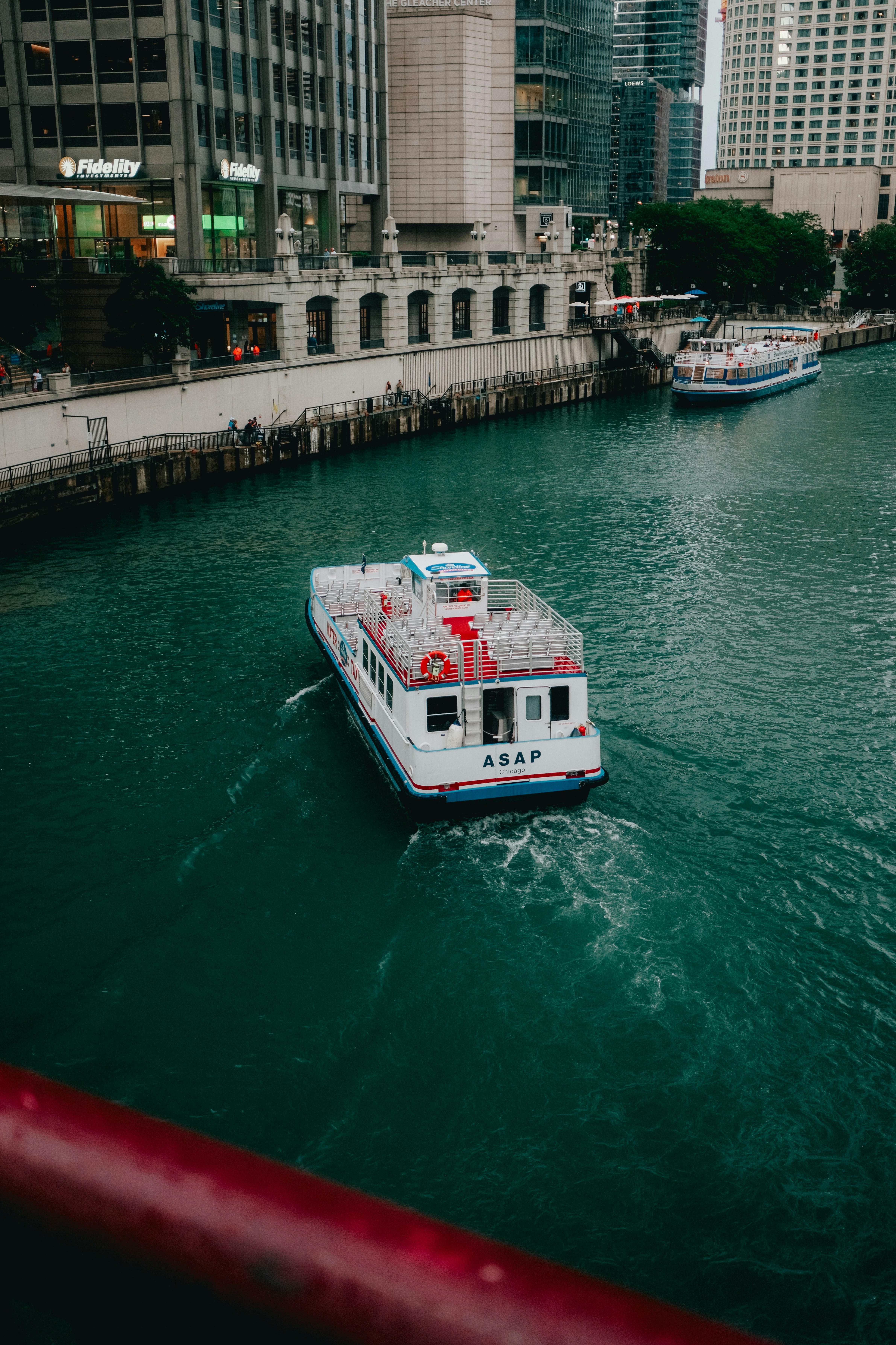 A white boat travels down a green river in a city.