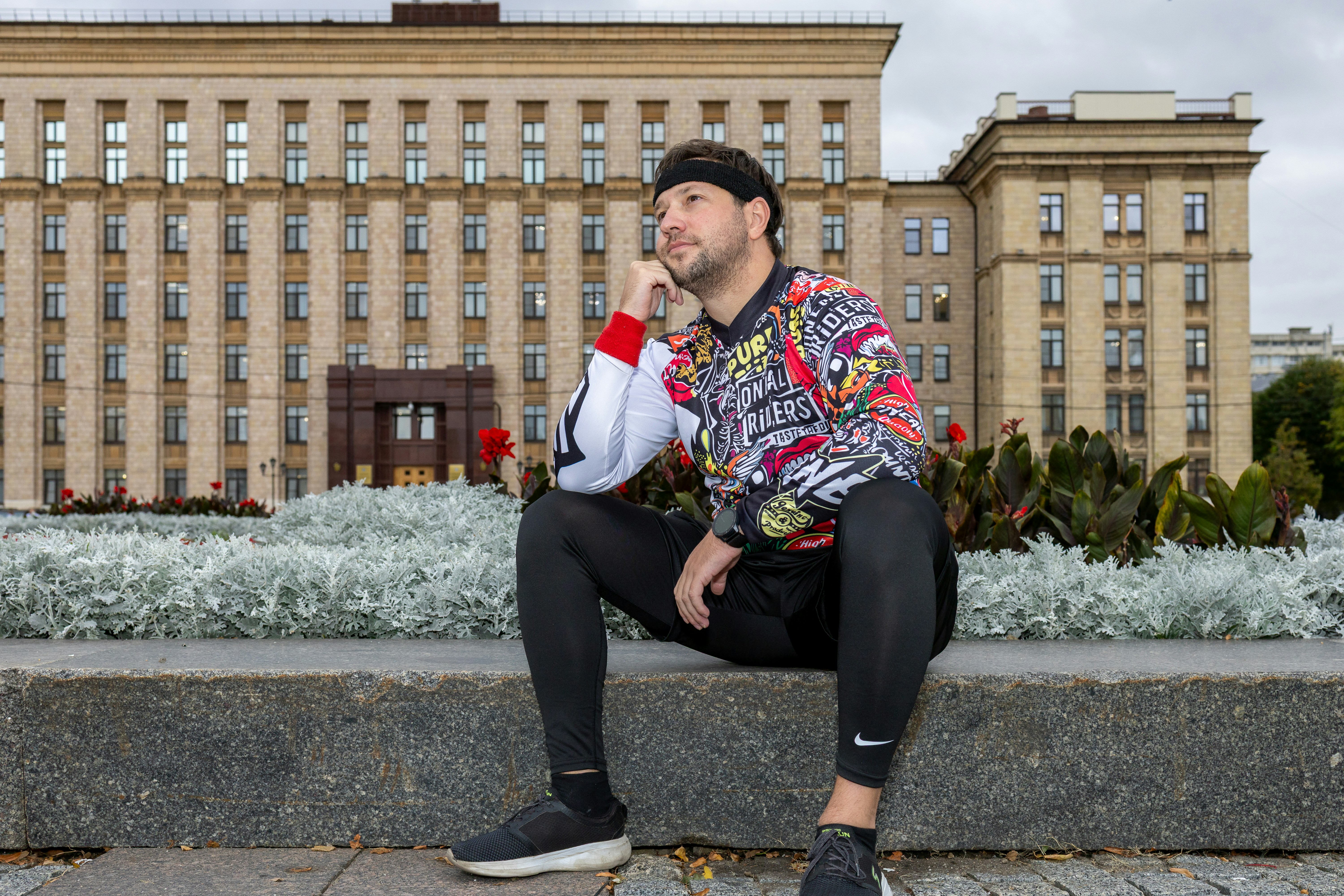 Man in colorful sweatshirt sitting in front of building