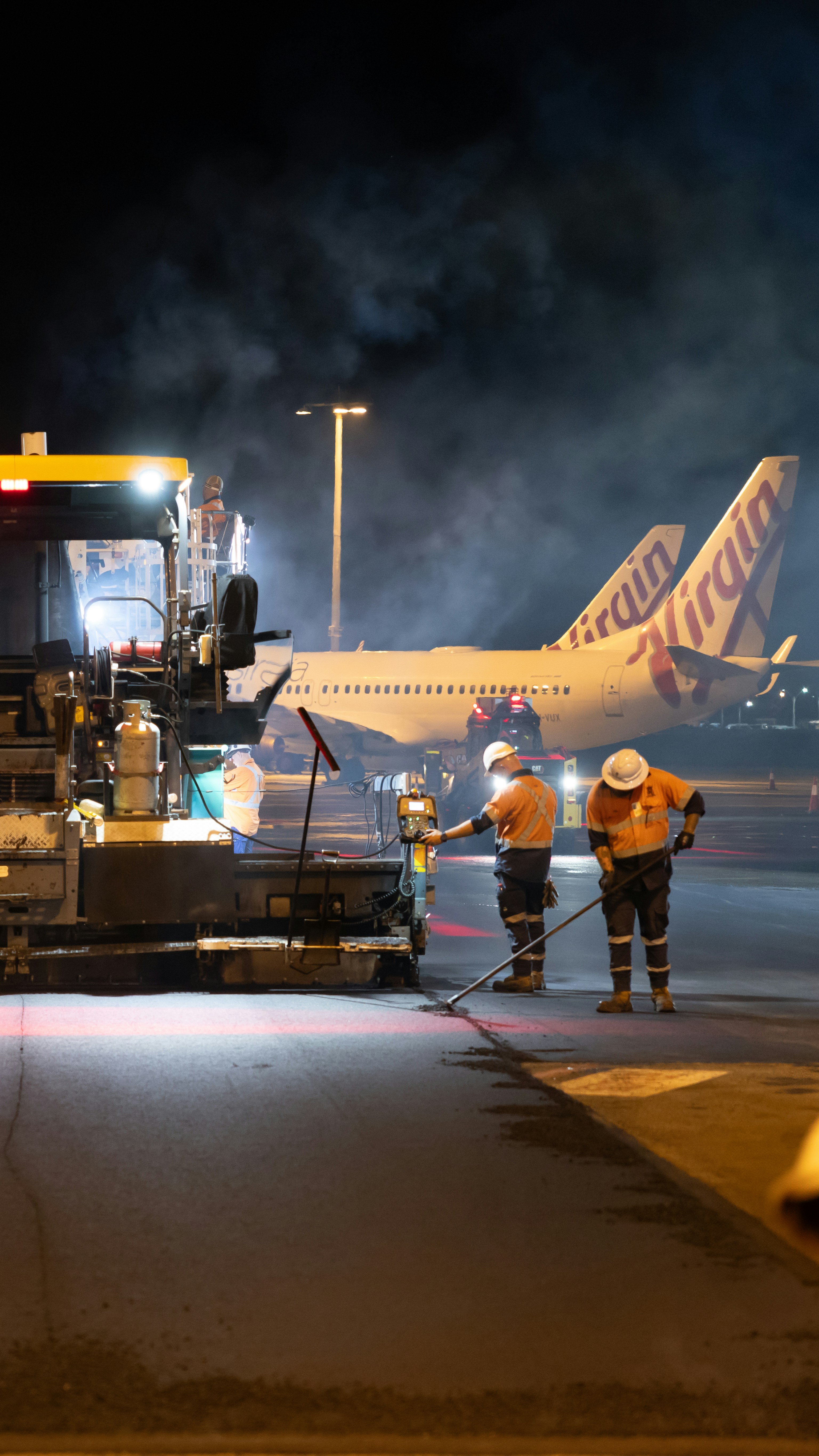 Airport workers paving tarmac near virgin australia airplanes at night