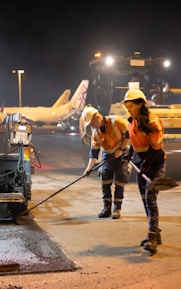 Workers paving tarmac at night with airplanes behind them.
