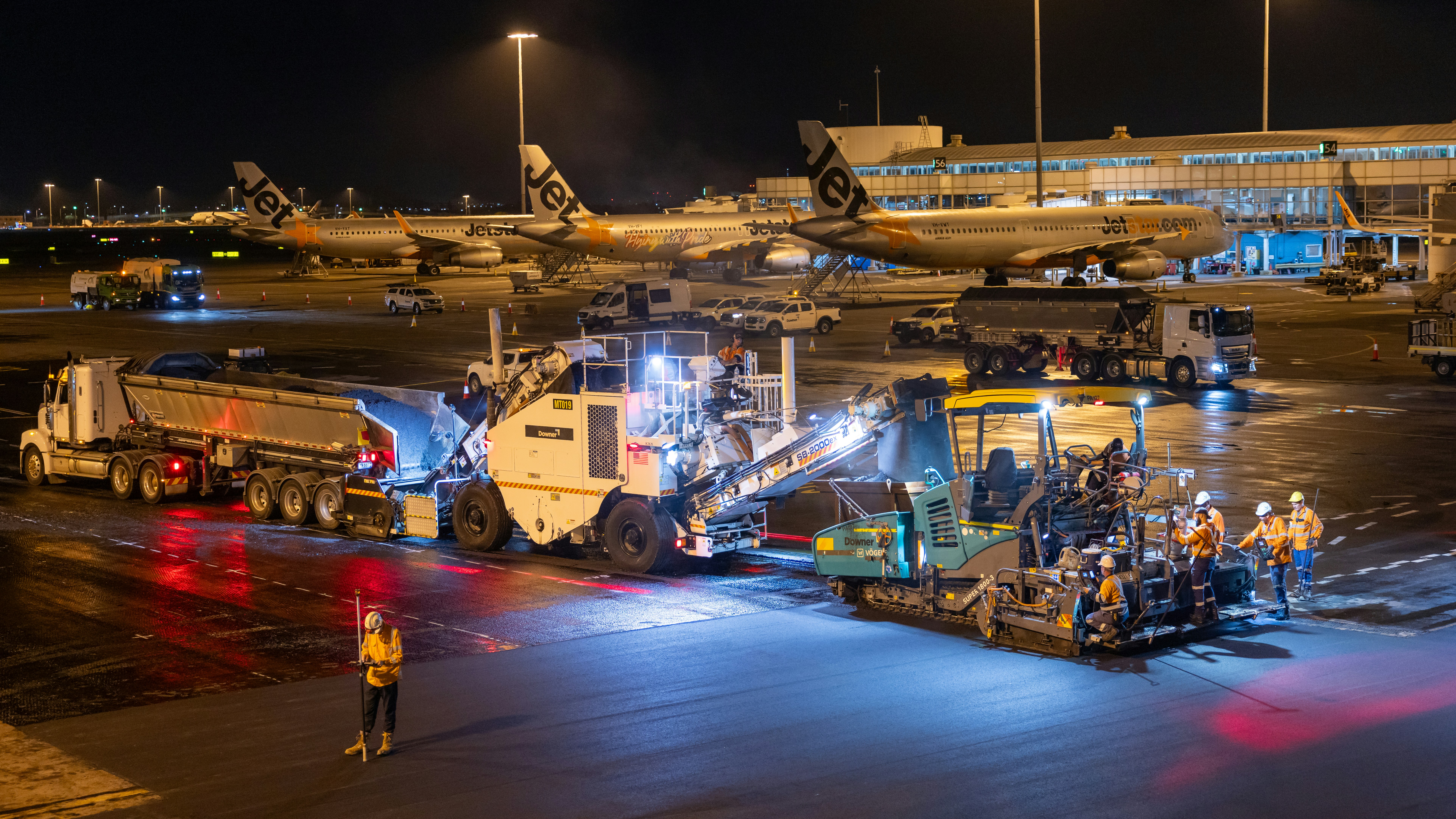 Airport tarmac resurfacing work at night with machinery and workers.