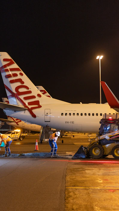 Airport workers repair tarmac near virgin australia airplanes at night.