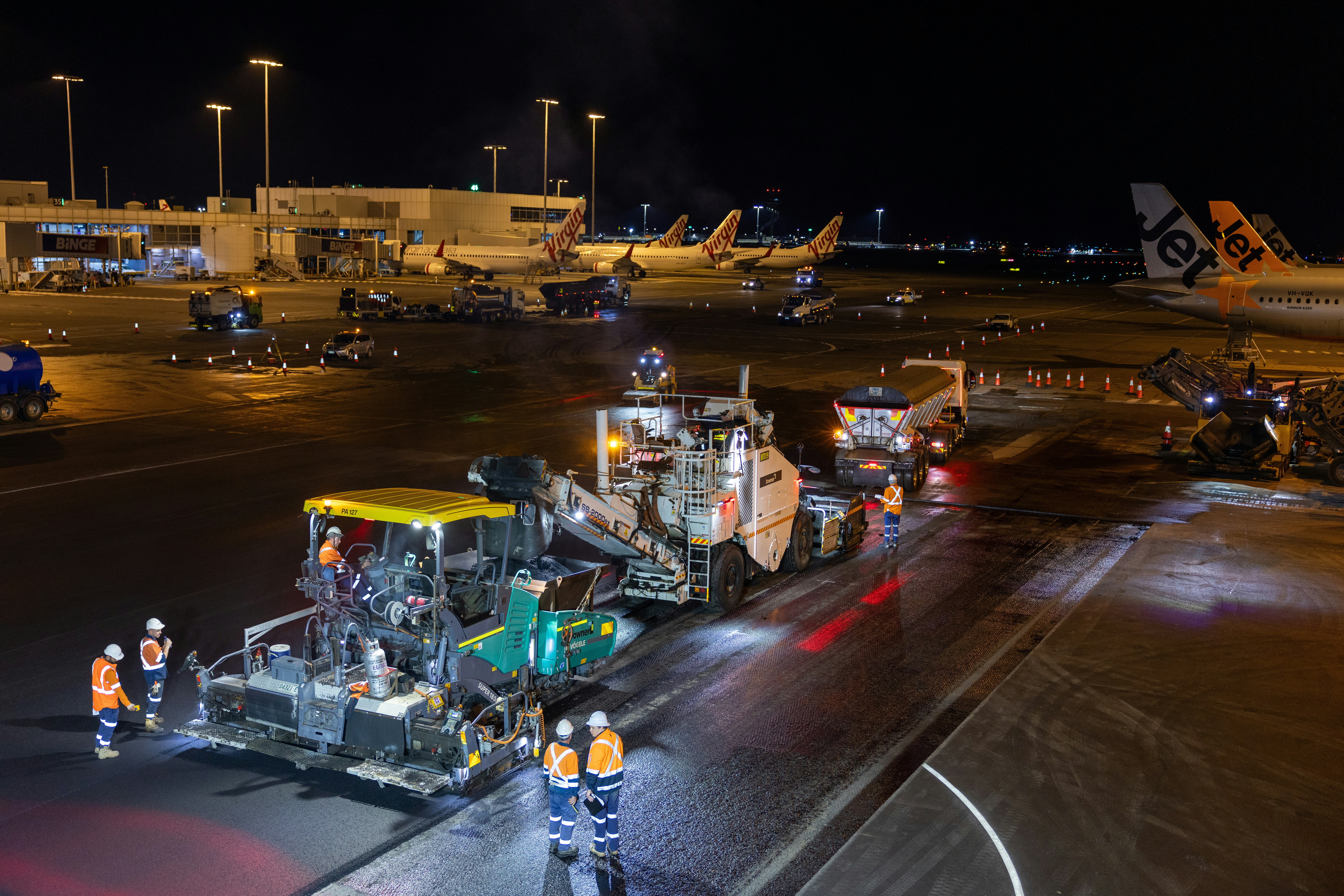 Airport runway resurfacing at night with heavy machinery