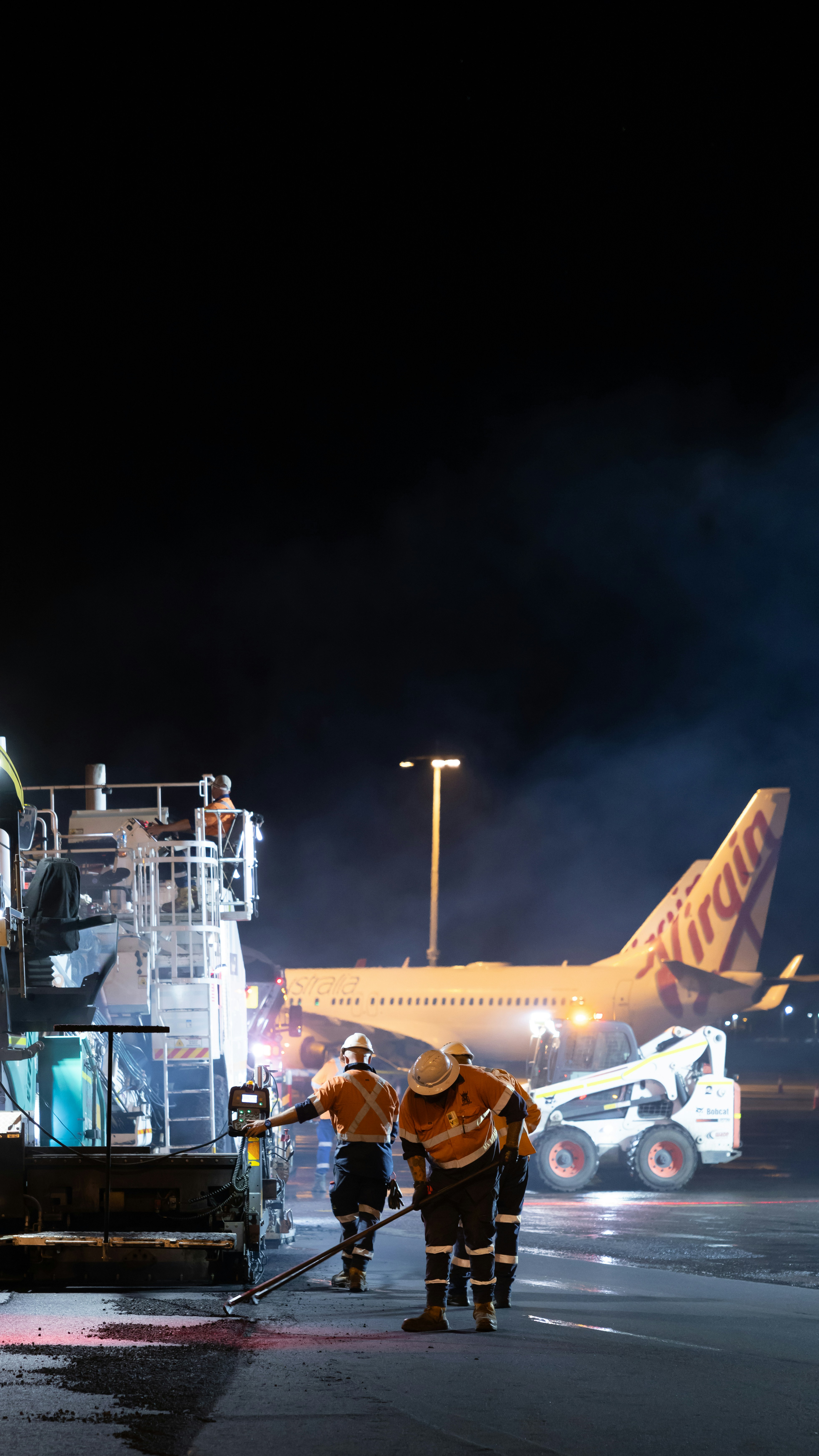 Workers repair tarmac near airplane at night
