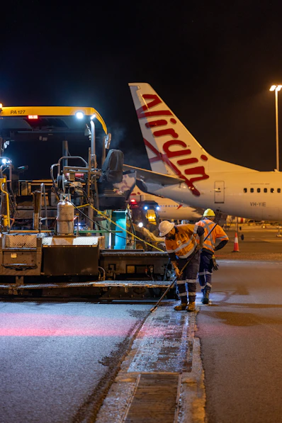 Workers repaving tarmac near virgin australia airplane at night