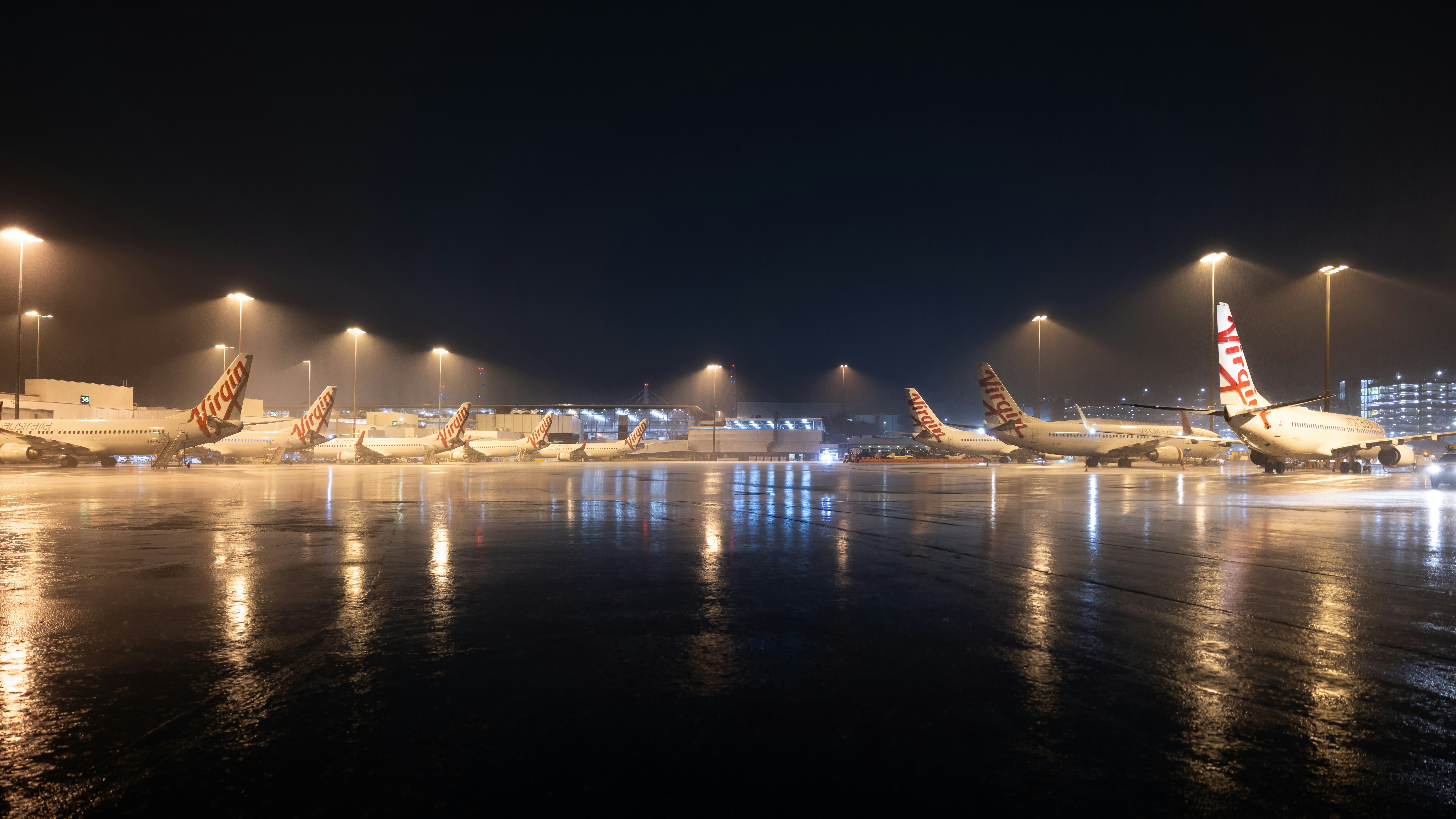 Airplanes parked on a wet tarmac at night.
