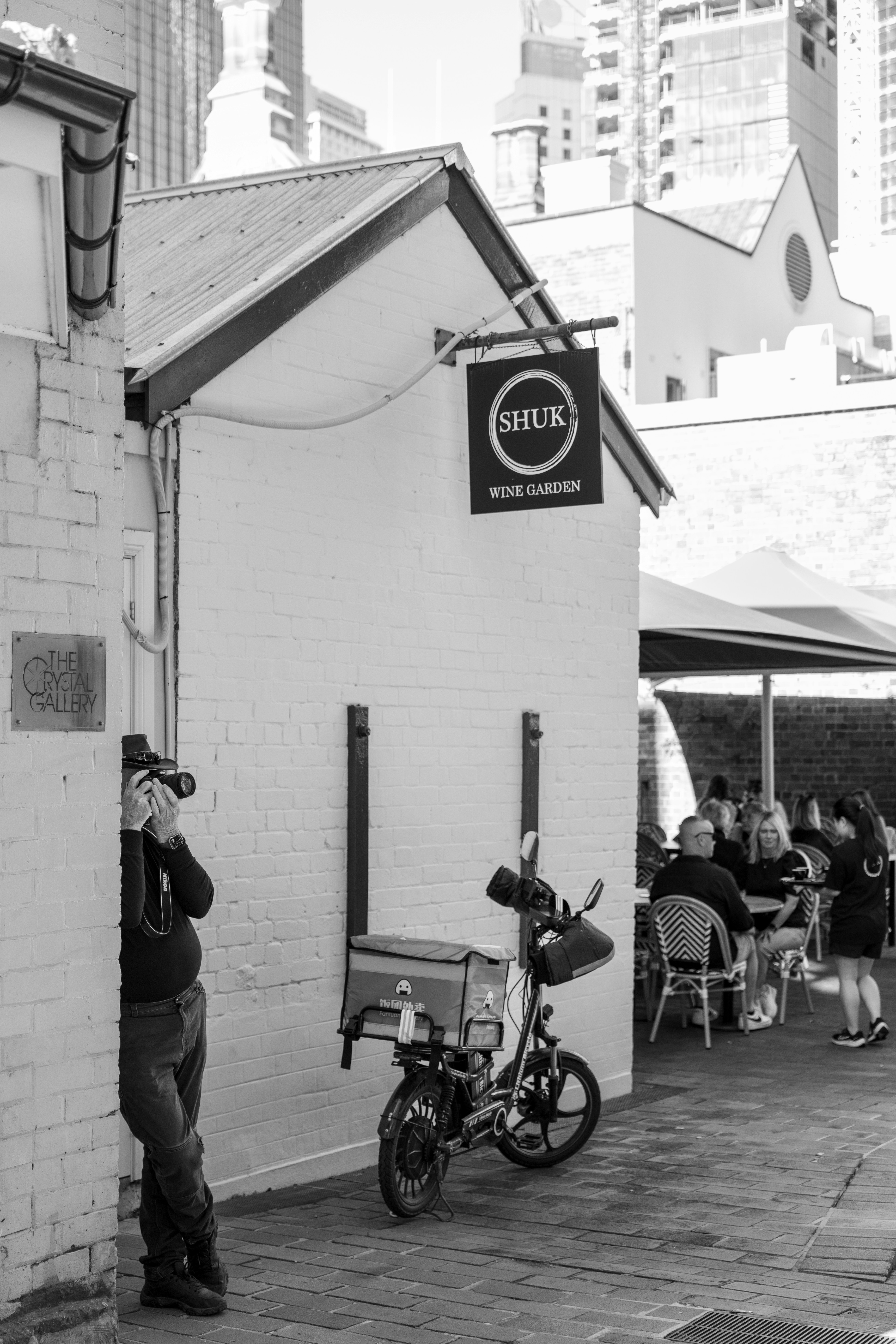 Man photographs building with shuk wine garden sign.