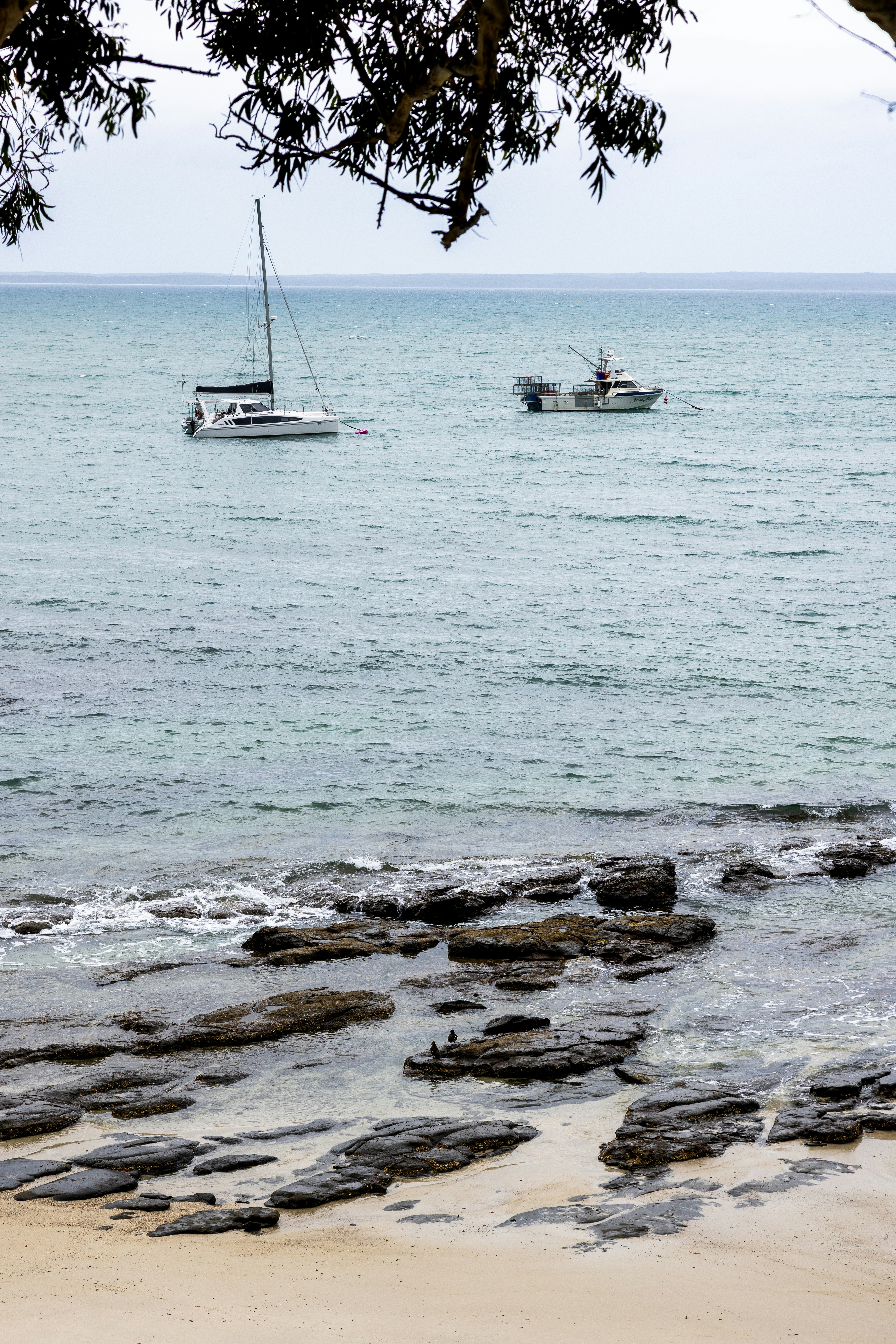 Two boats sail on the ocean near rocky shore.