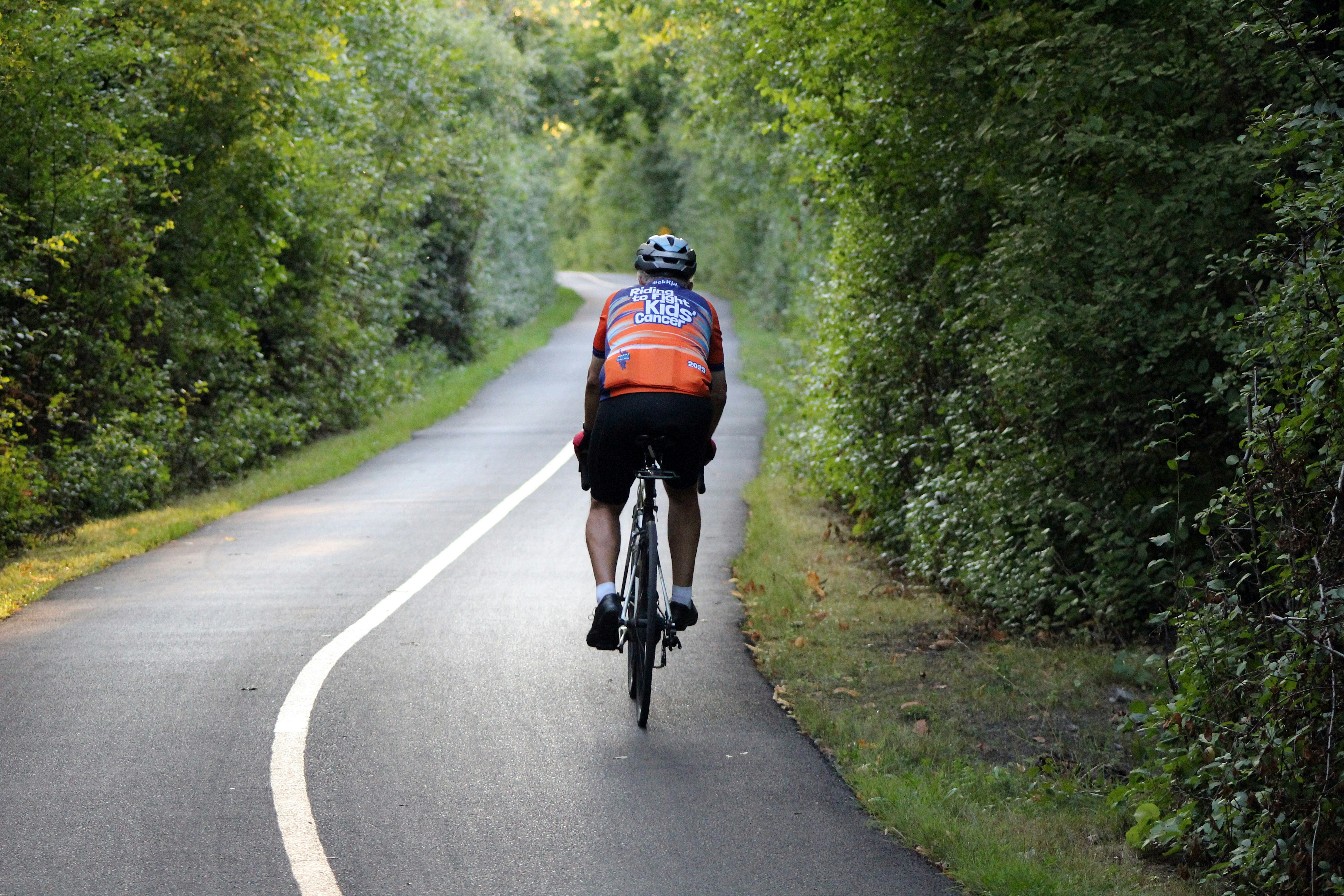 Person cycling on a paved path through trees