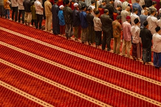 A group of men stand in prayer on a red carpet.