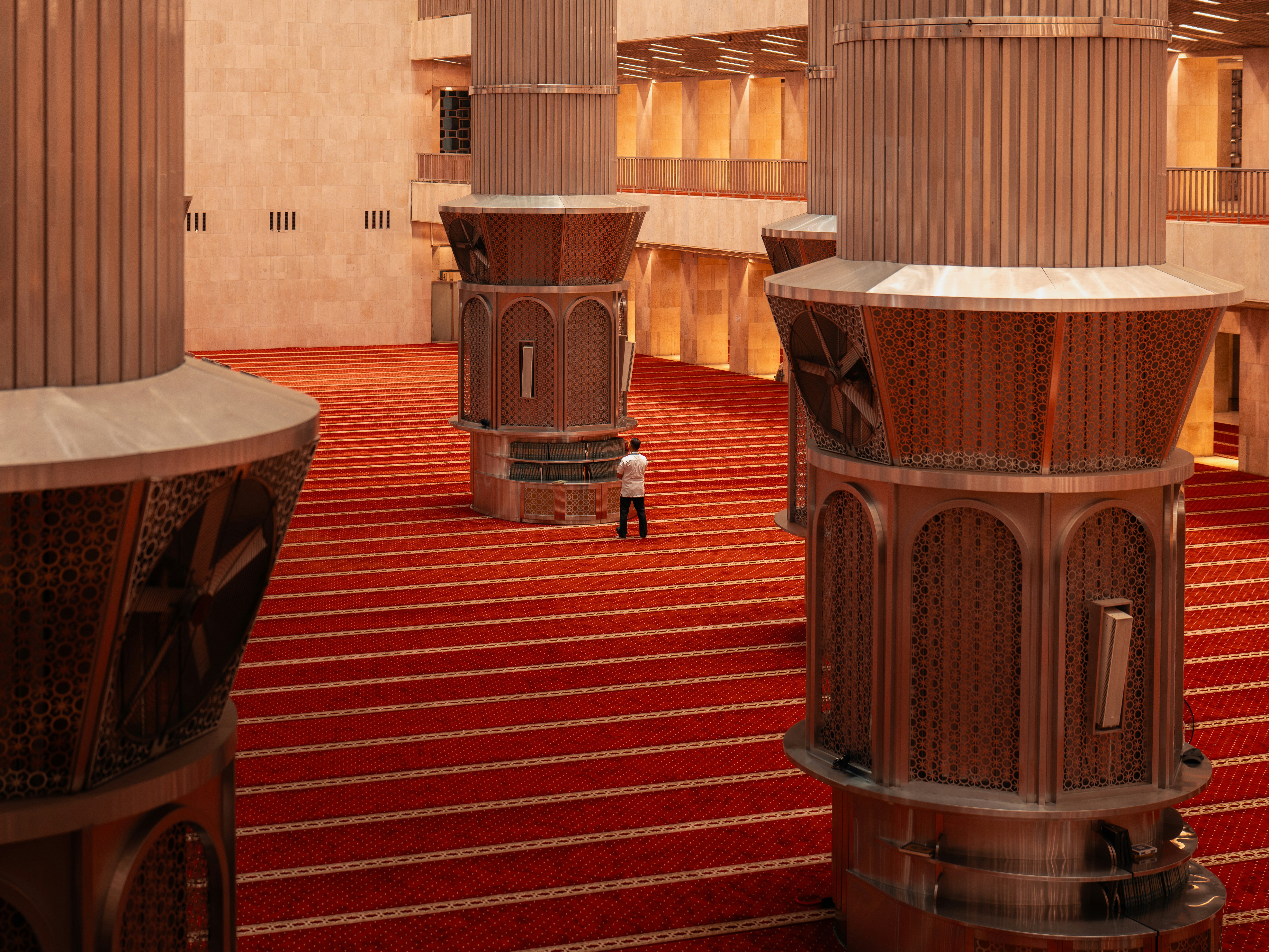 A lone man stands in a large hall with red carpet.