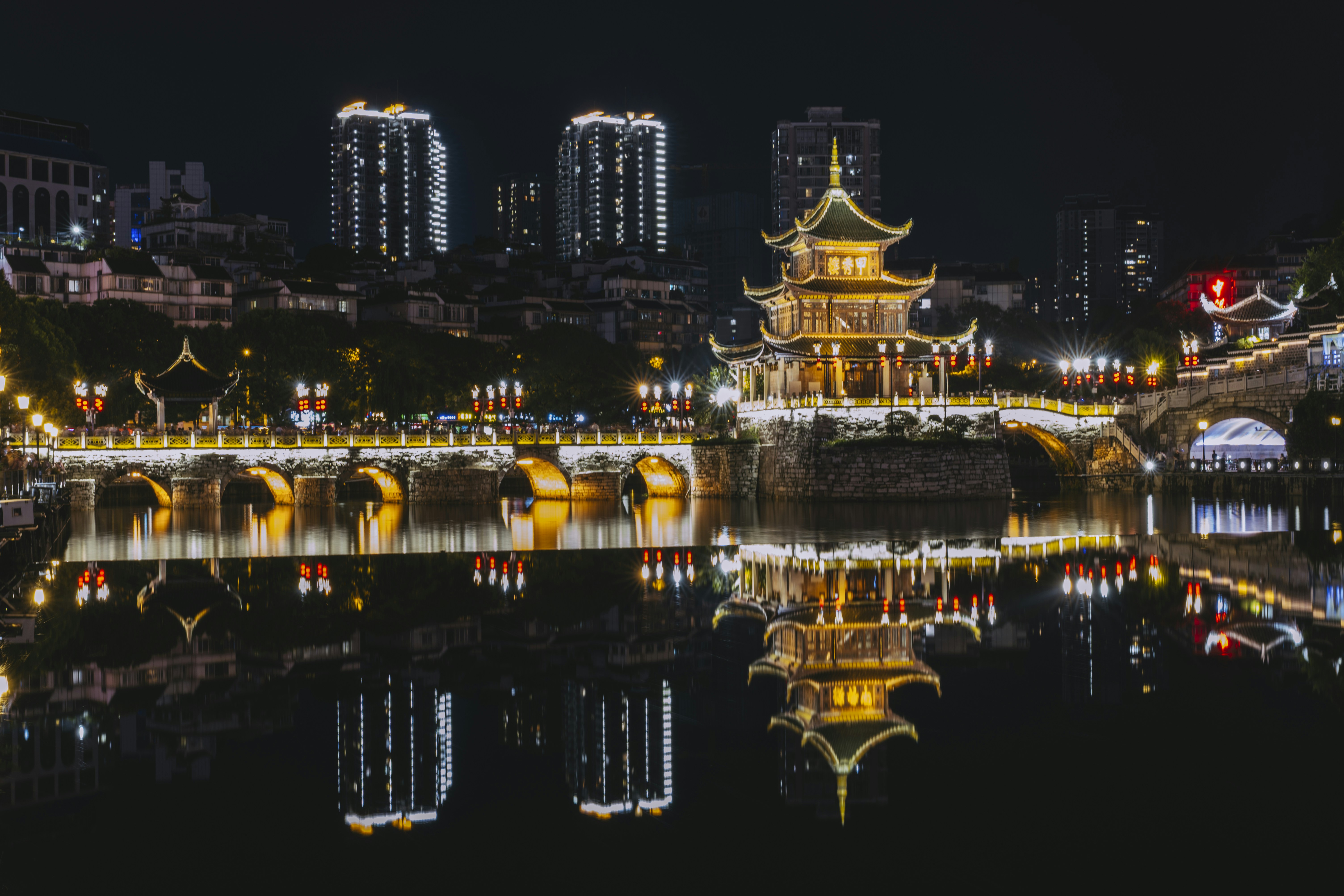 Illuminated traditional building and bridges over water at night.