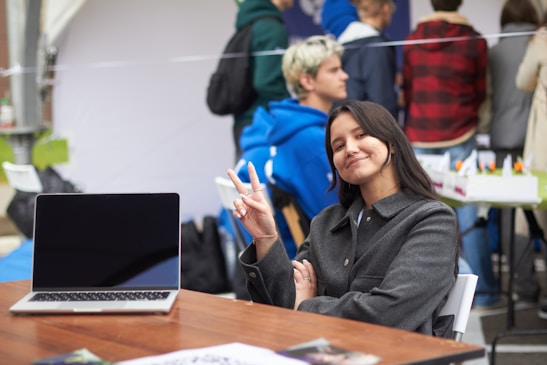 A smiling woman holds up two fingers near a laptop.