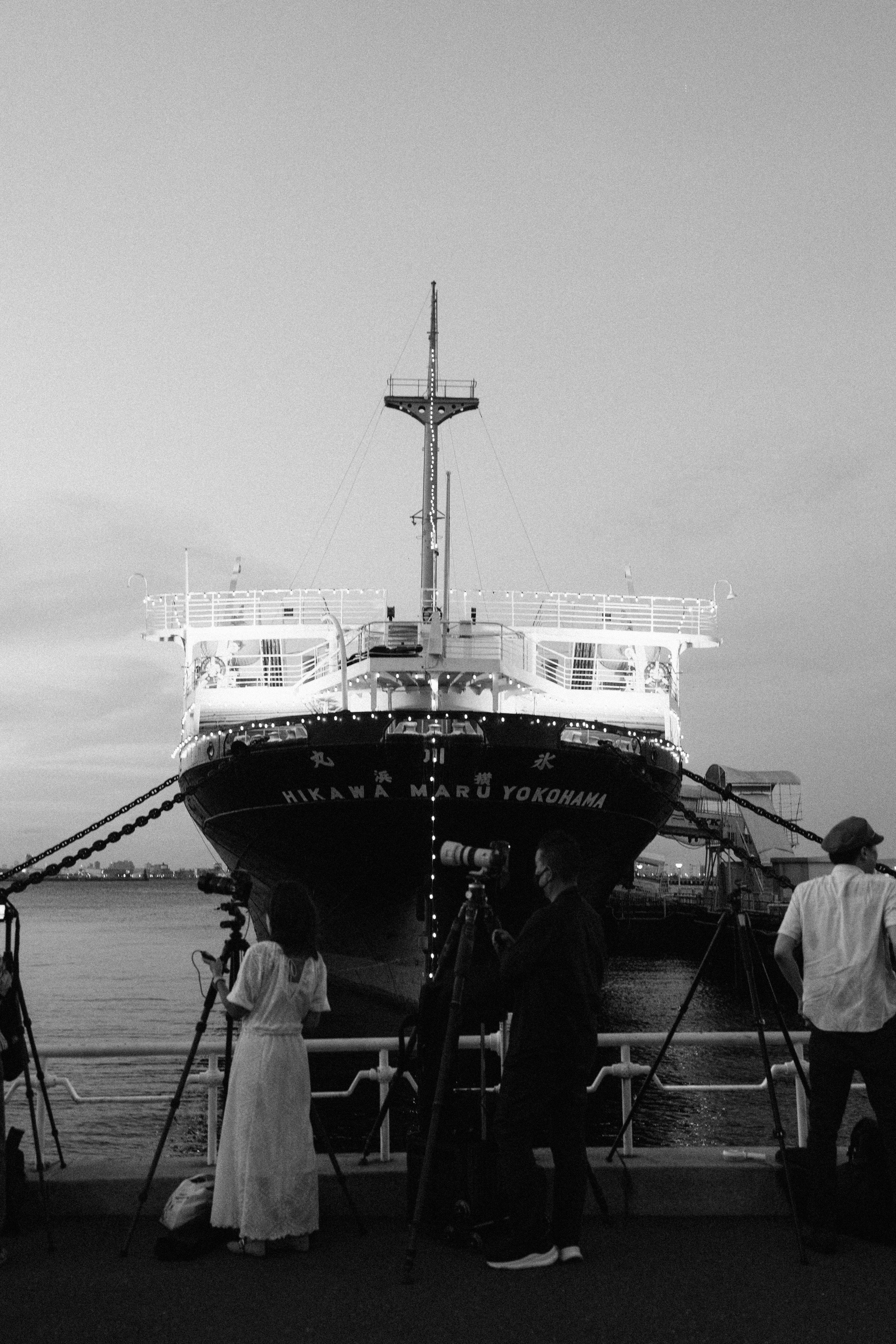 People filming a large ship docked at a pier