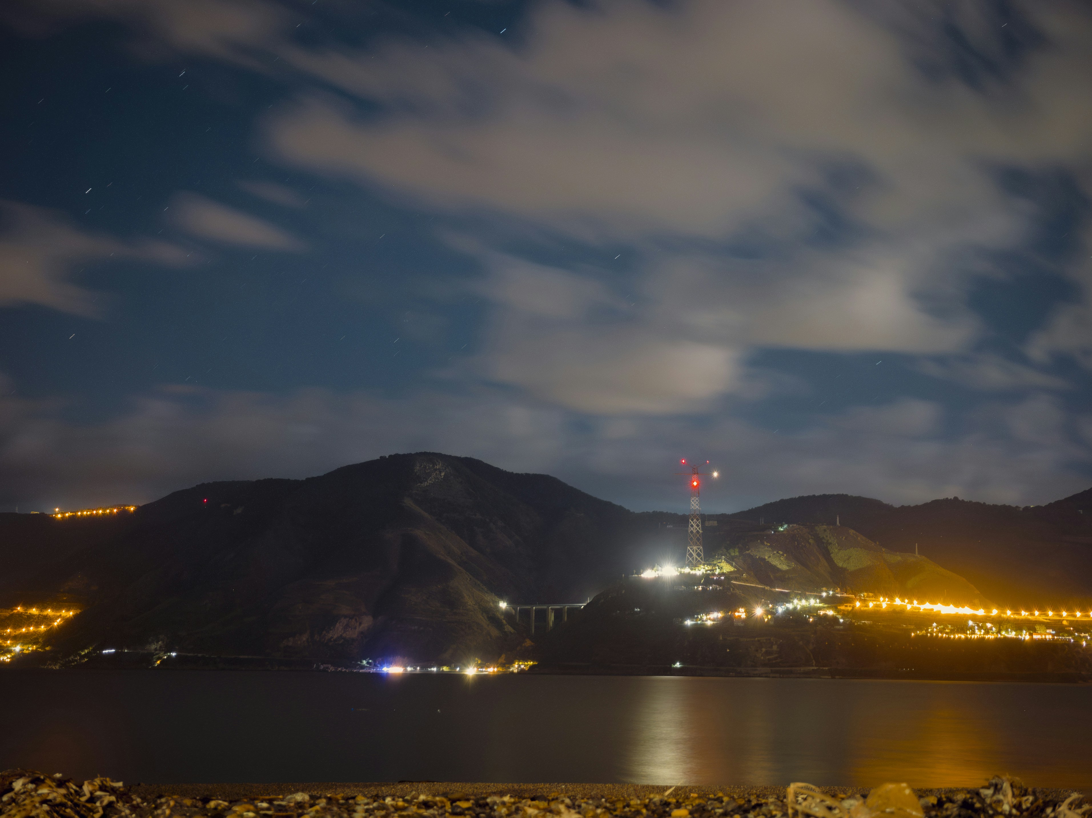 Nighttime cityscape with distant mountains and reflective water.