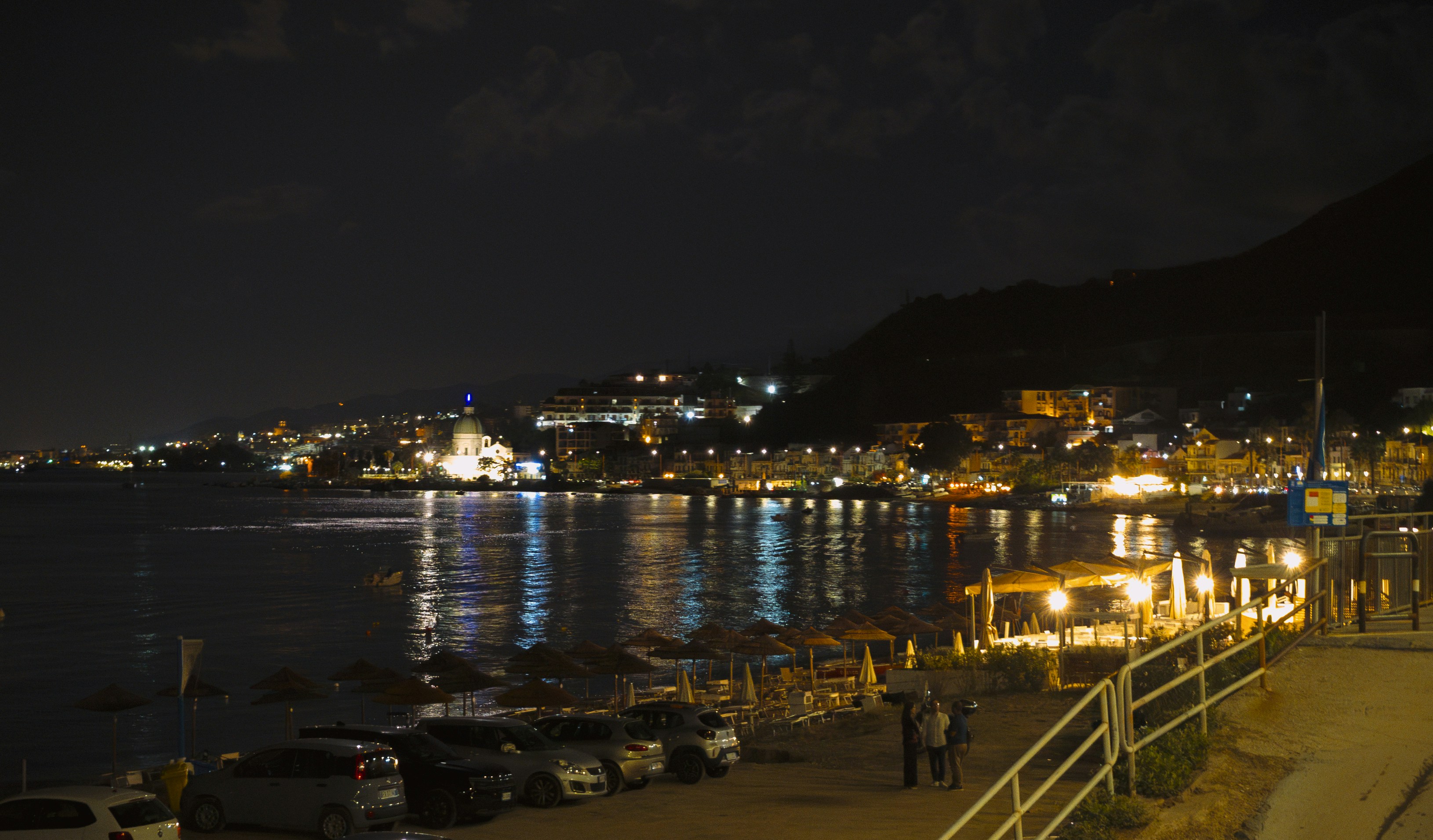 Coastal town illuminated at night with reflections on water.