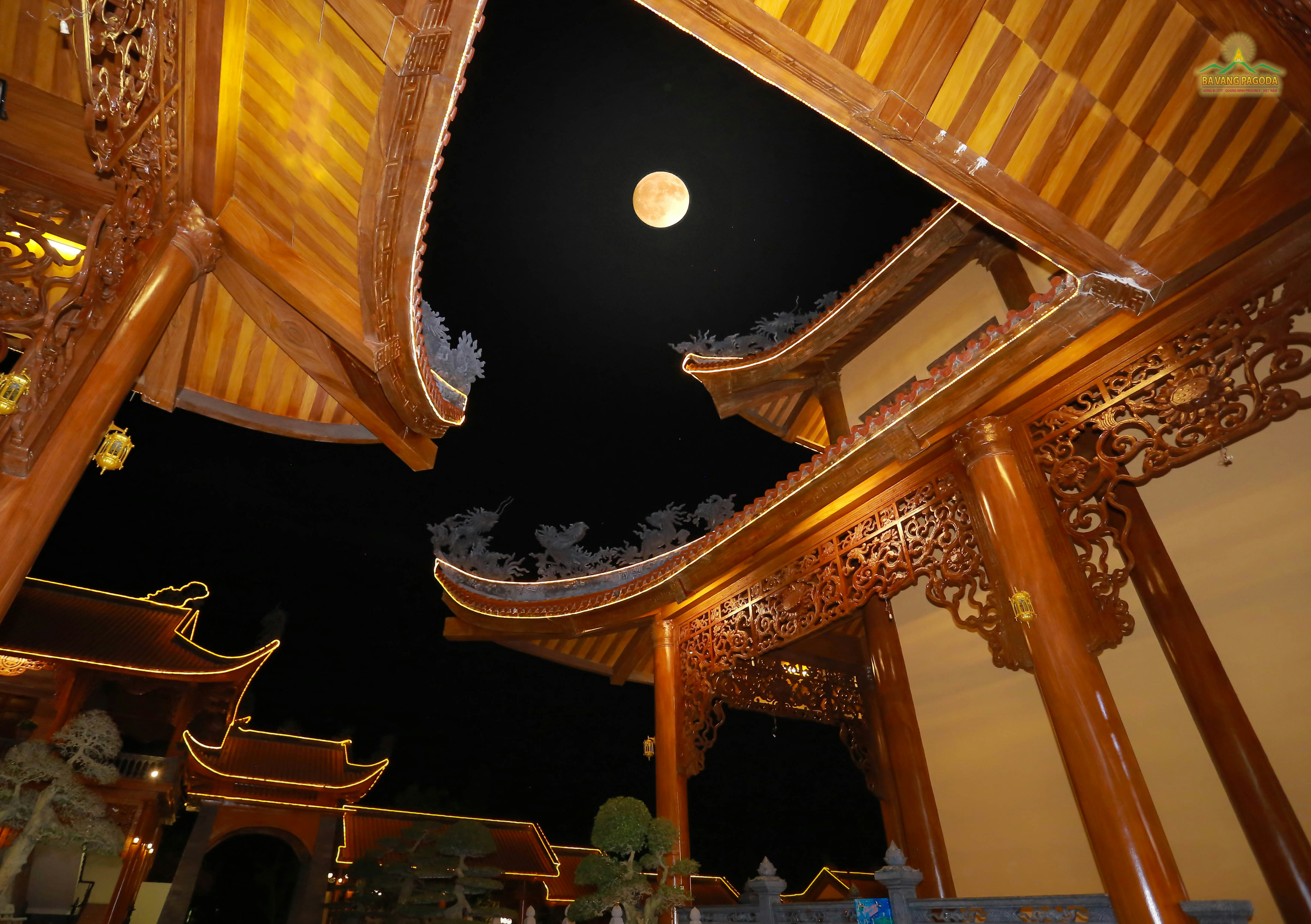 Full moon visible through ornate wooden temple architecture.