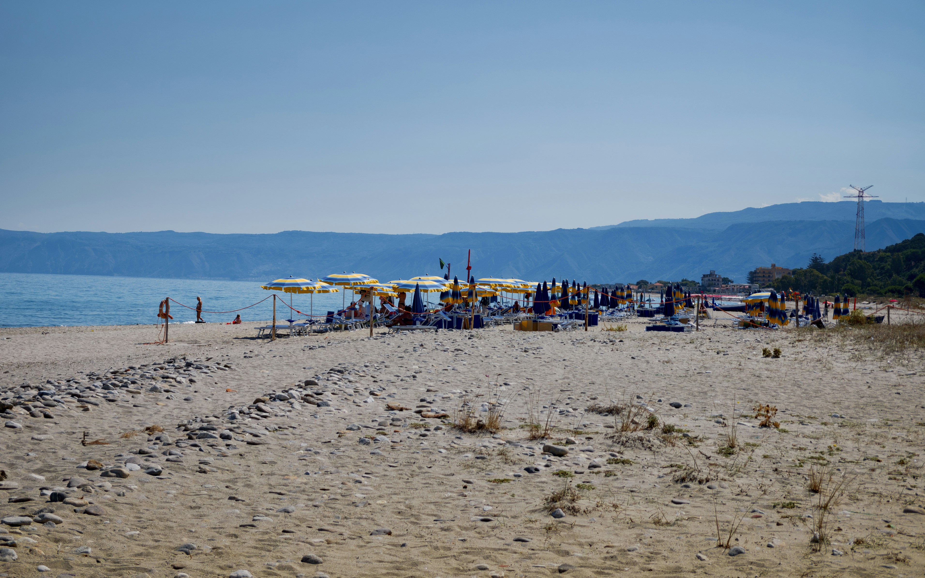 A sunny beach with umbrellas and distant hills.