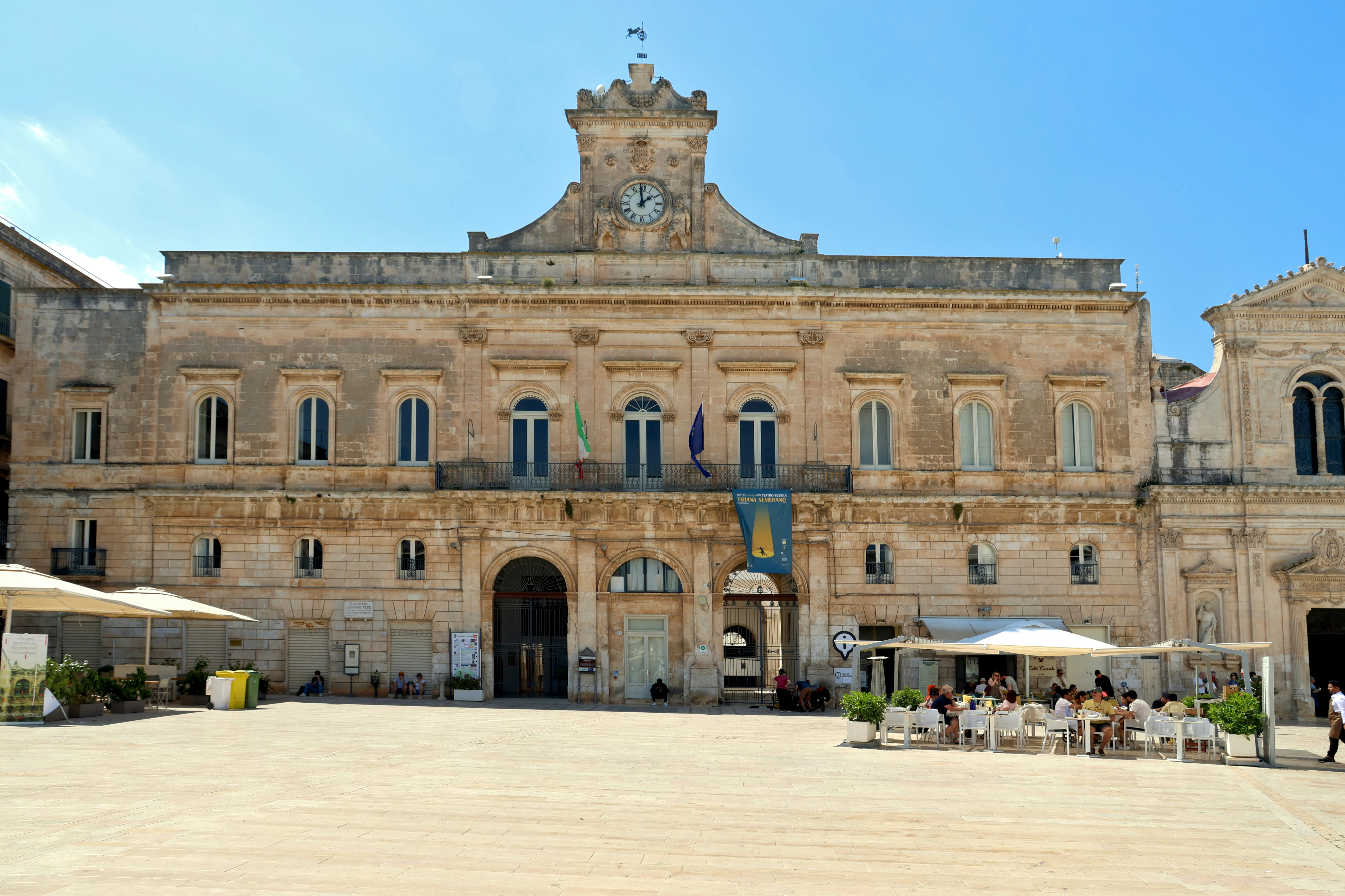 Grand ornate building with clock tower in sunny plaza.