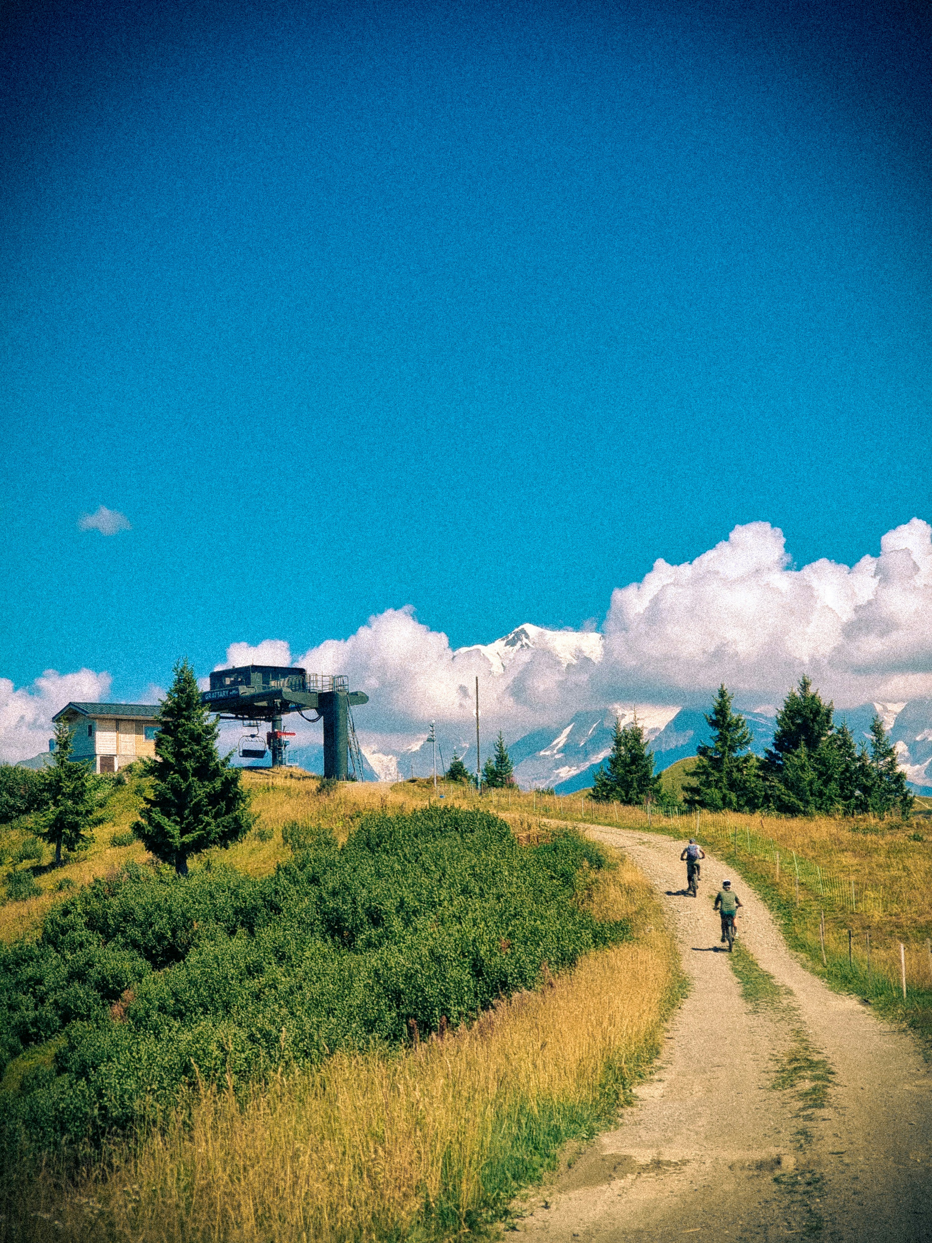 Two people hike on a mountain path near a ski lift.