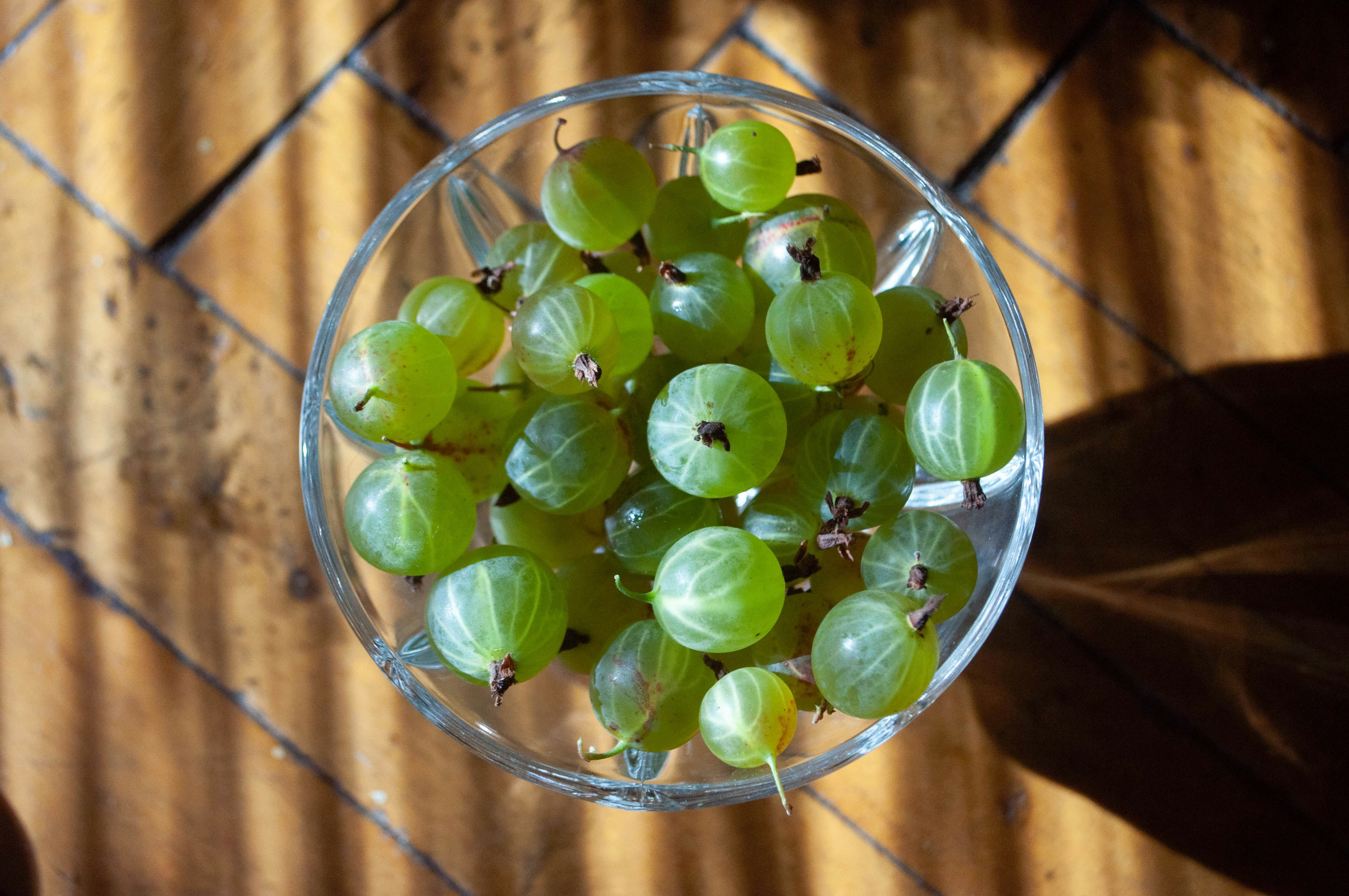 Bowl of fresh green gooseberries on a wooden surface