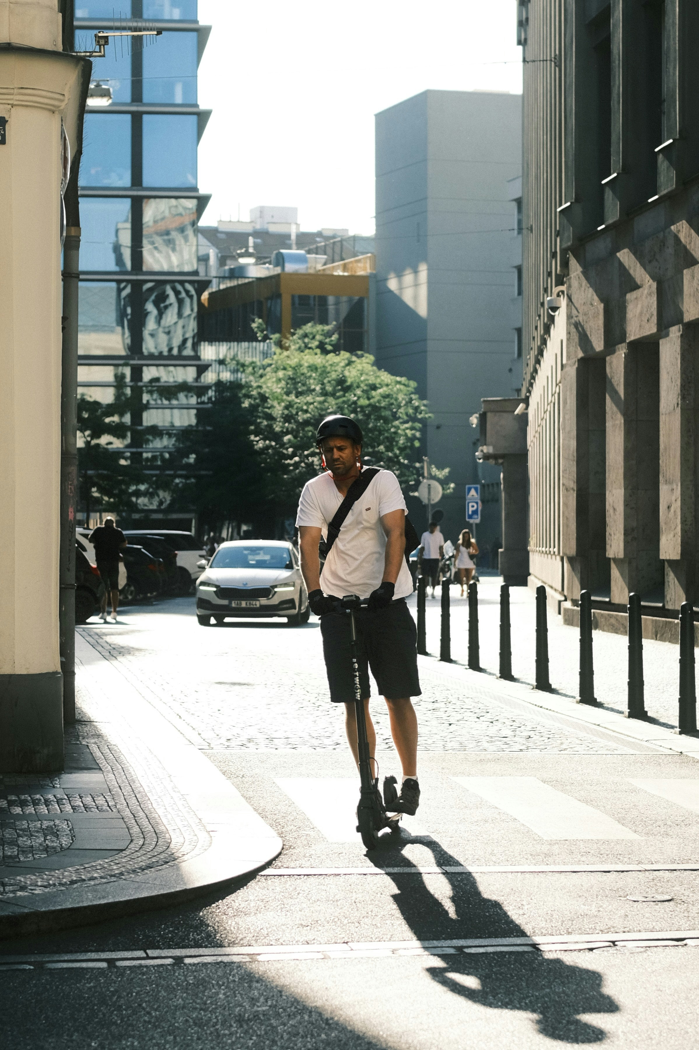 Man riding an electric scooter down a sunny street.