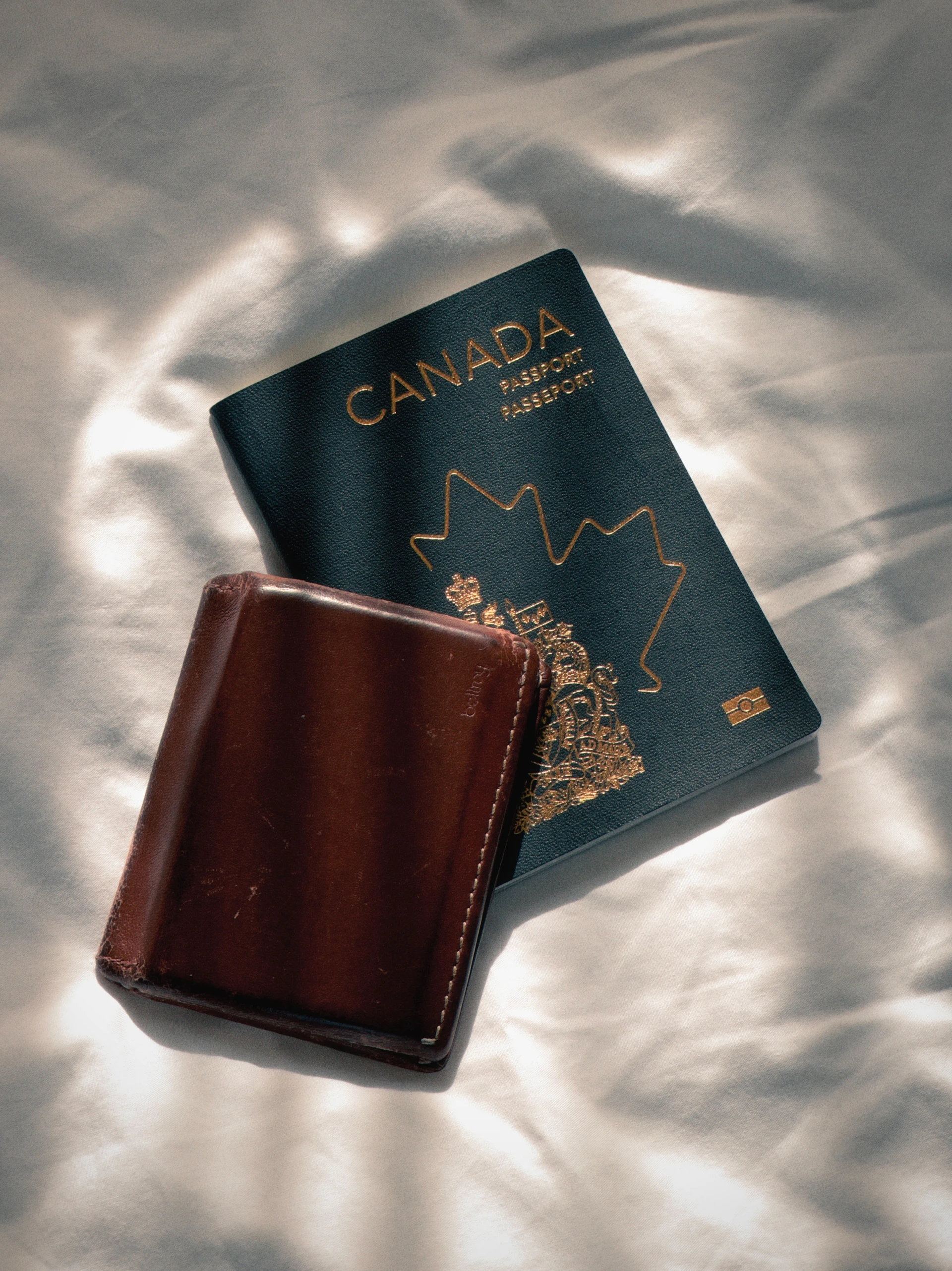 Canadian passport and brown leather wallet on white fabric