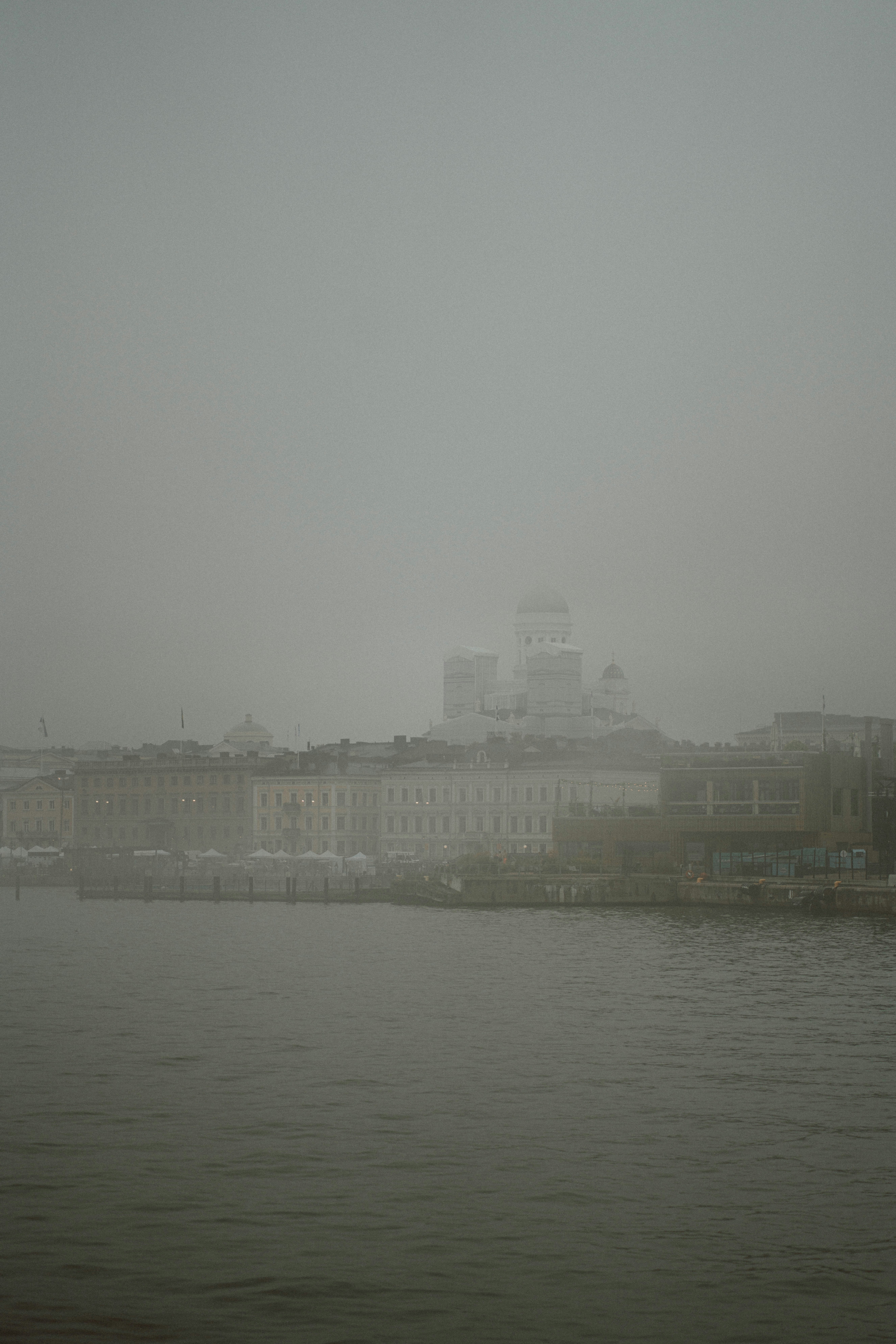 White cathedral emerges from thick fog over water.