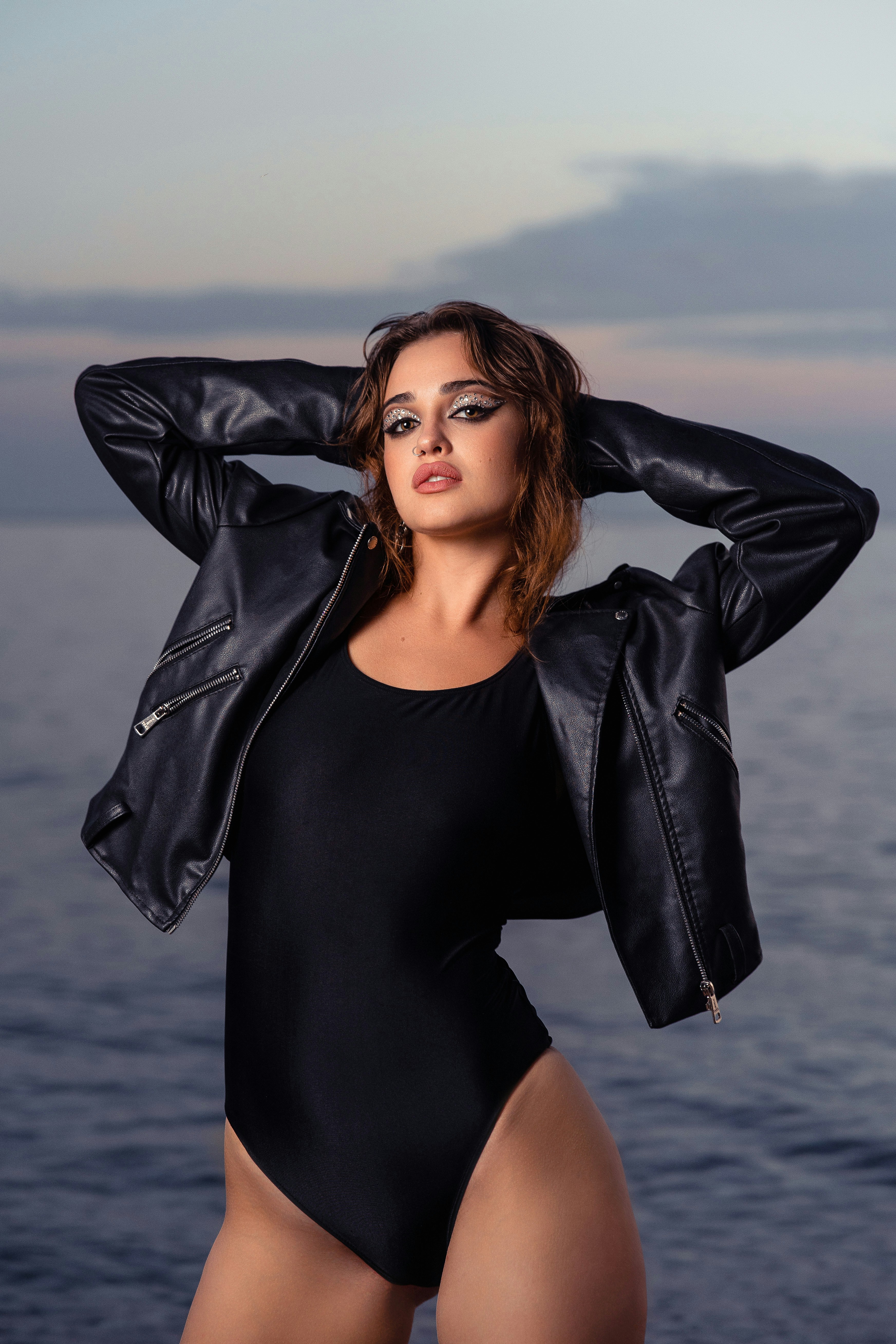 Woman in black bodysuit and leather jacket by the sea
