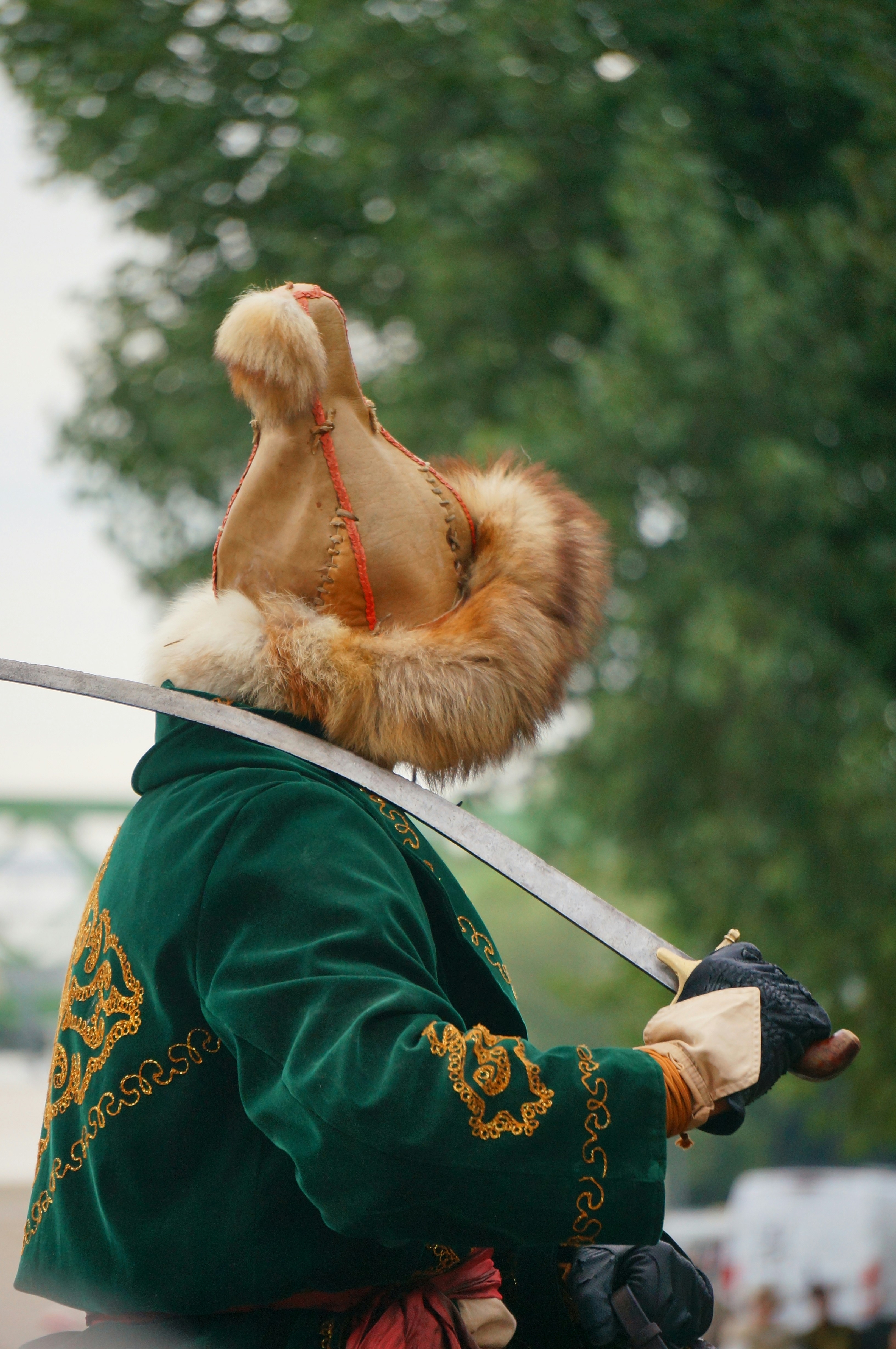 Man in ornate green jacket and fur hat holds sword