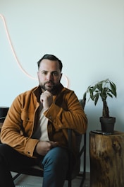 Man in a brown jacket sitting in a chair.