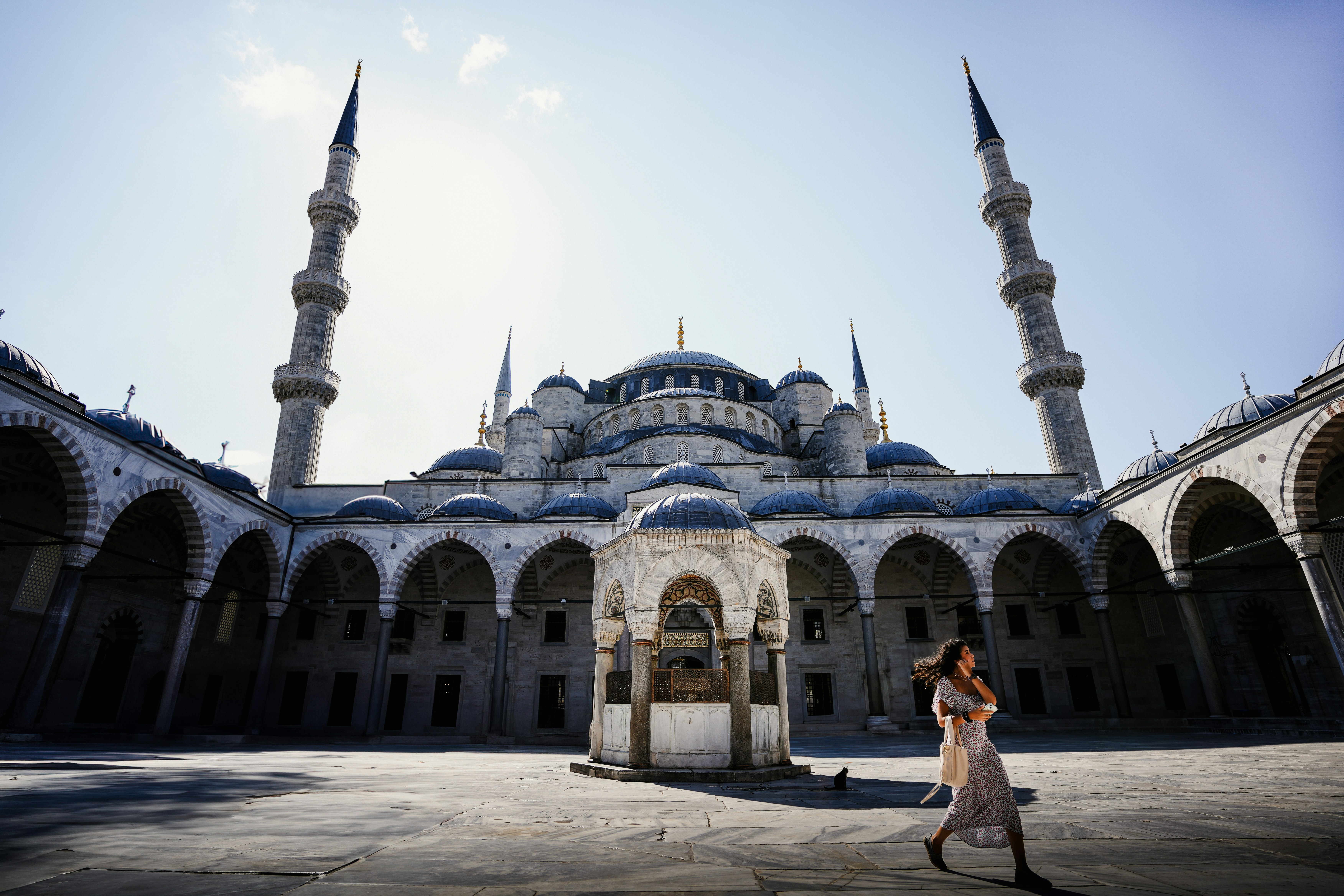 Woman walks in front of a grand mosque with minarets.