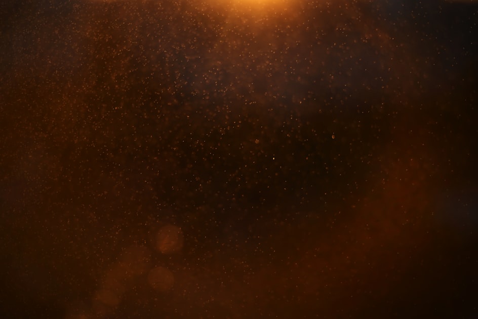 Fine dust particles floating in warm indoor light, illustrating airborne particulates that CRI-certified vacuums are engineered to capture
