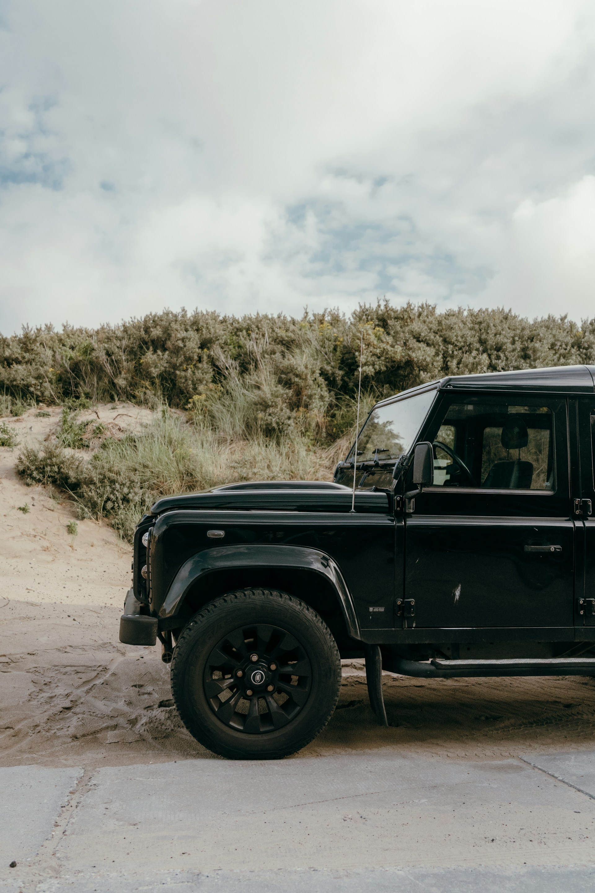 Black suv parked on a sandy path near dunes