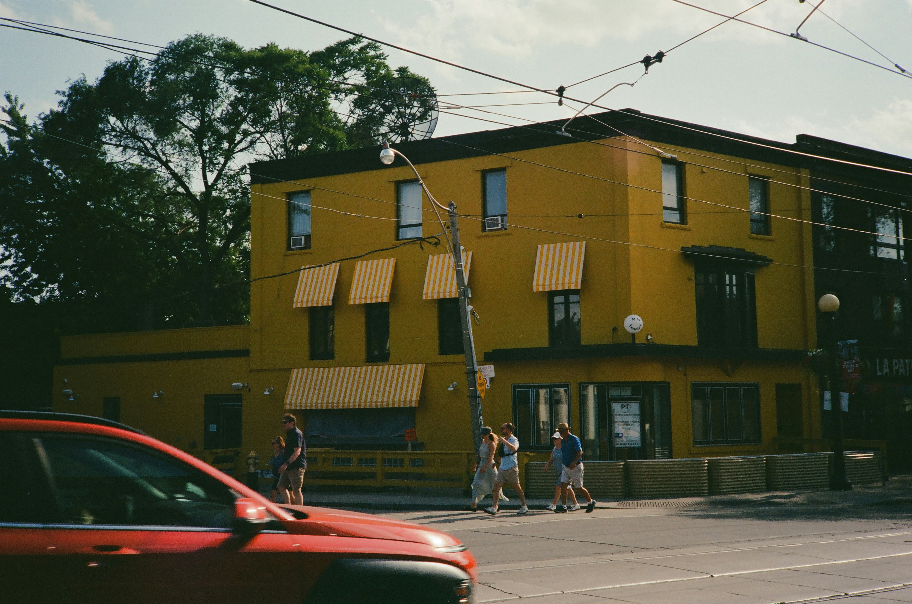 People walk past a bright yellow building on a sunny day.