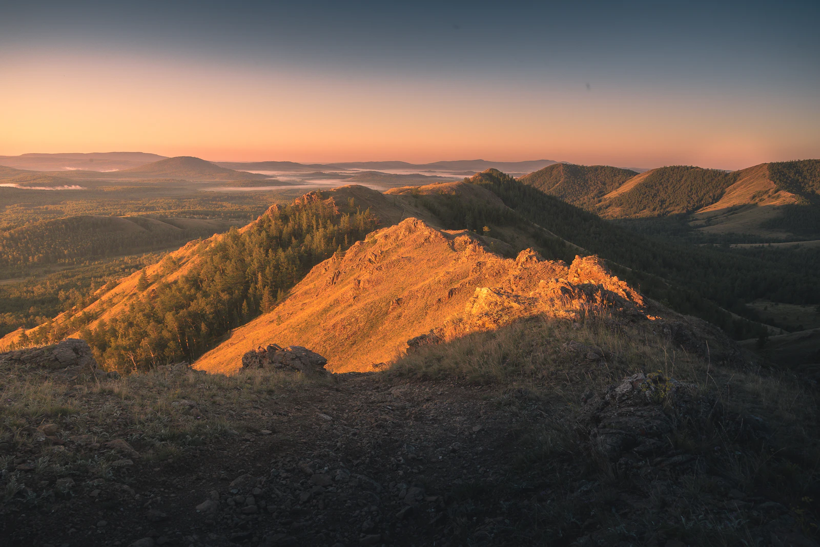 Soft golden light and mist settling over quiet mountains at dawn