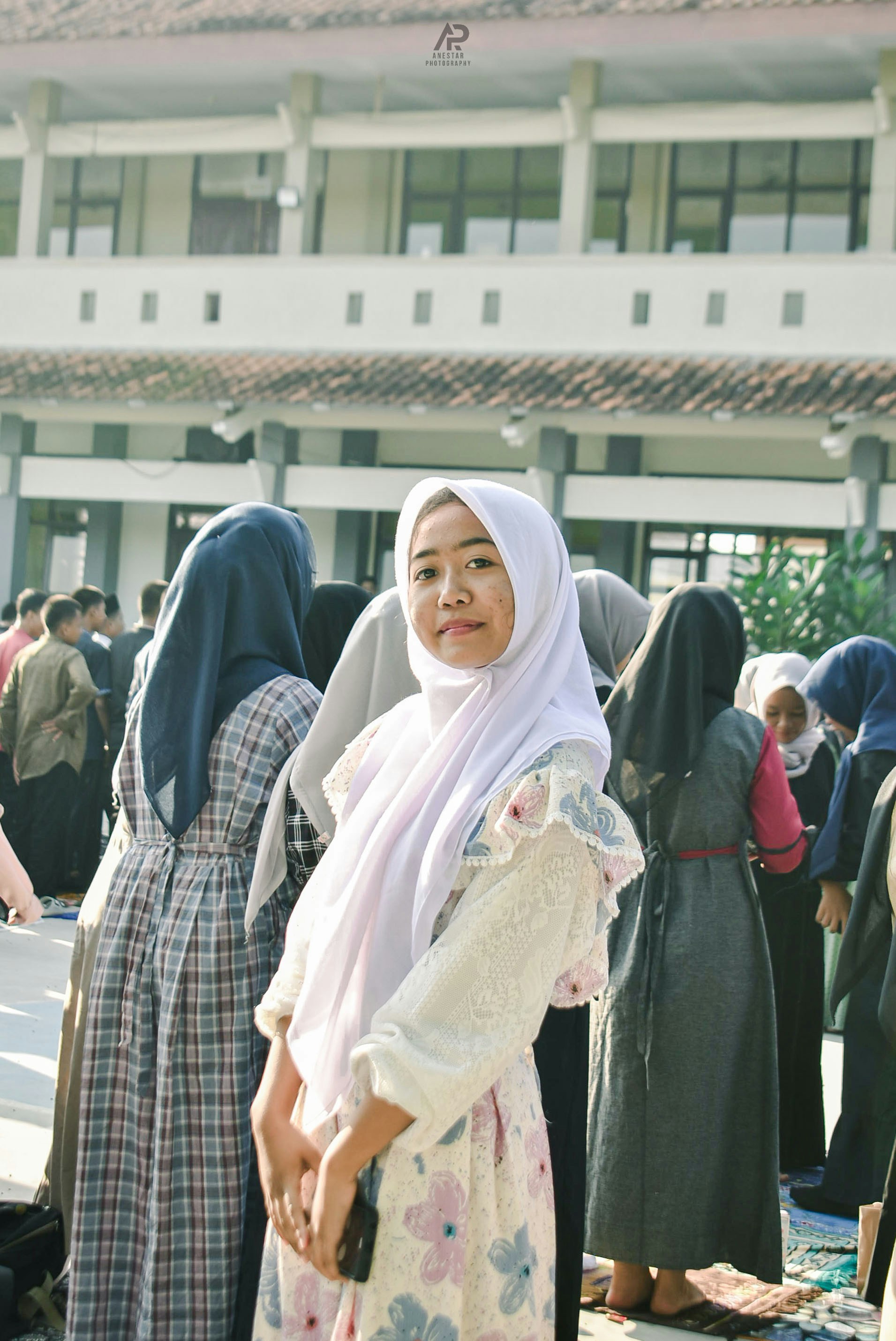 Young woman in hijab smiles in front of building